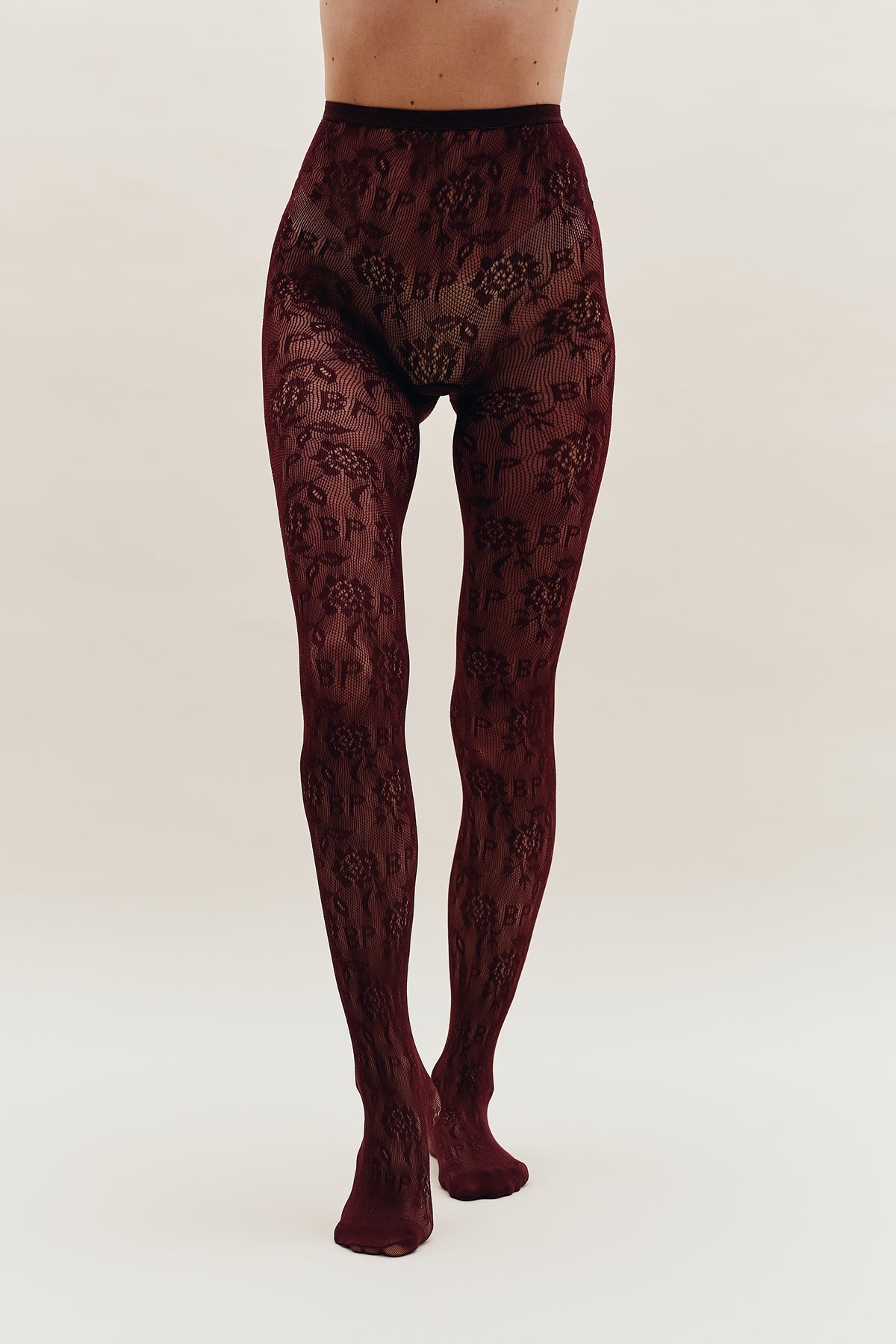 Front view of burgundy tights with an all-over black floral mesh pattern, shown on a model from waist to feet.