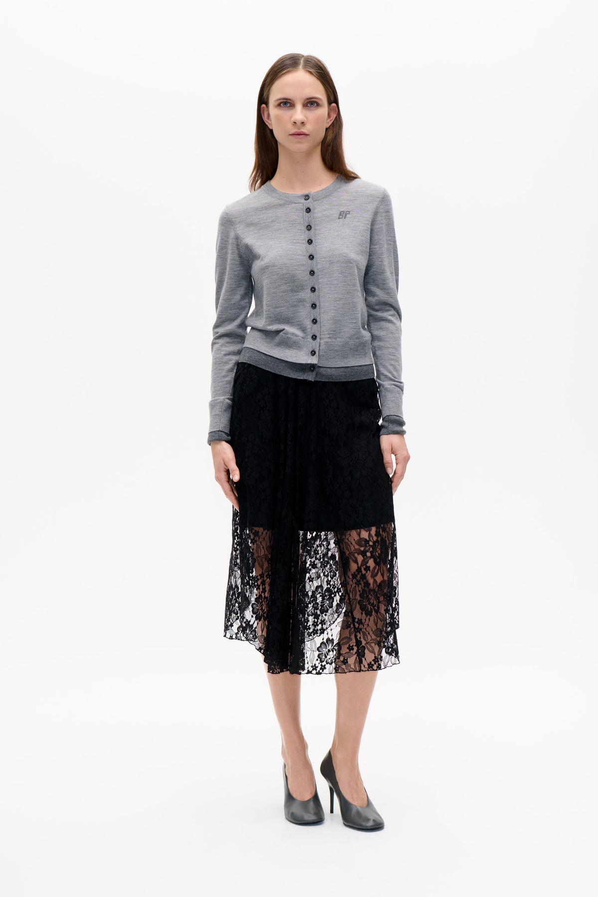 Front view of a model wearing a grey button-front cardigan with a small chest monogram and a black floral lace skirt.