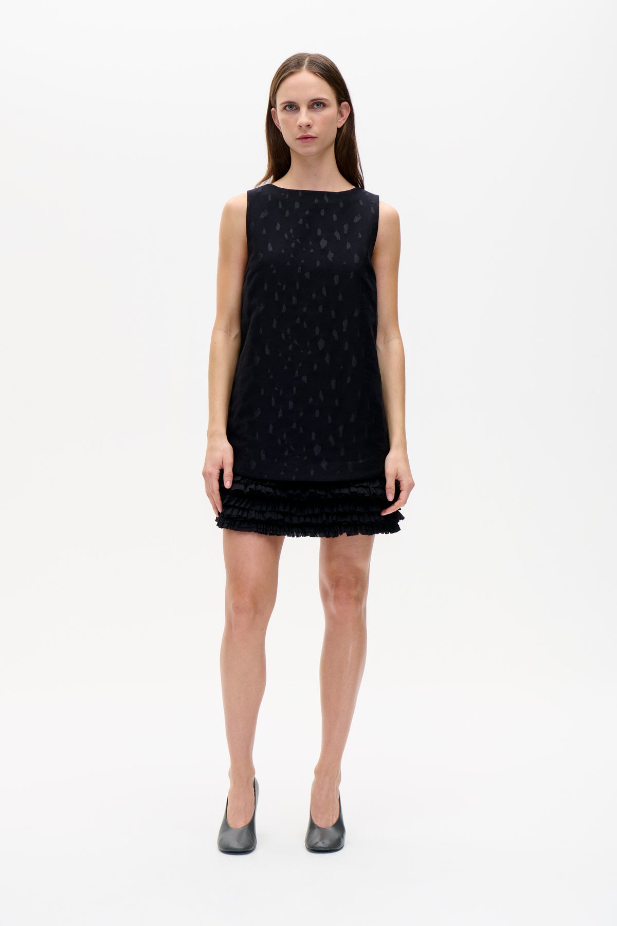 Front view of a black sleeveless mini dress with a subtle tonal abstract pattern and layered ruffle hem.