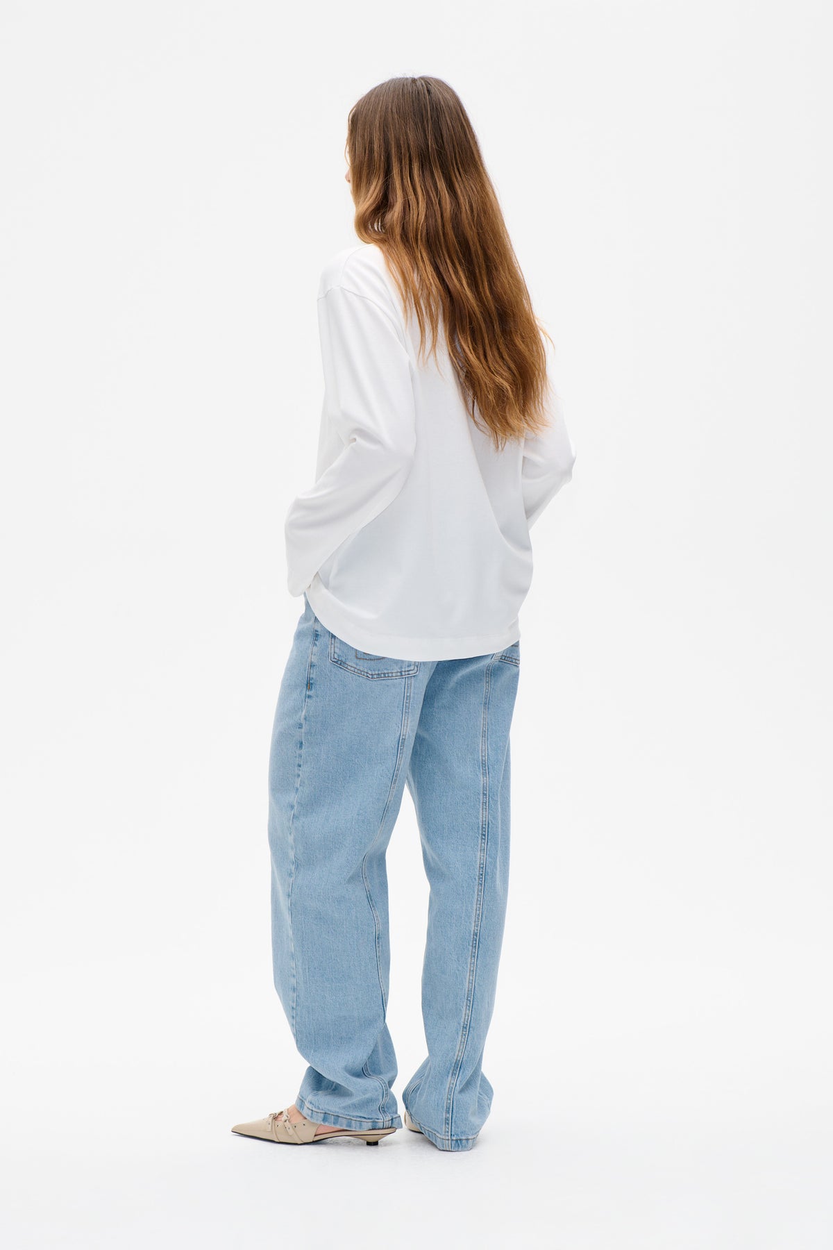 Rear view of a model wearing a white long-sleeved sweatshirt and light-wash wide-leg jeans.