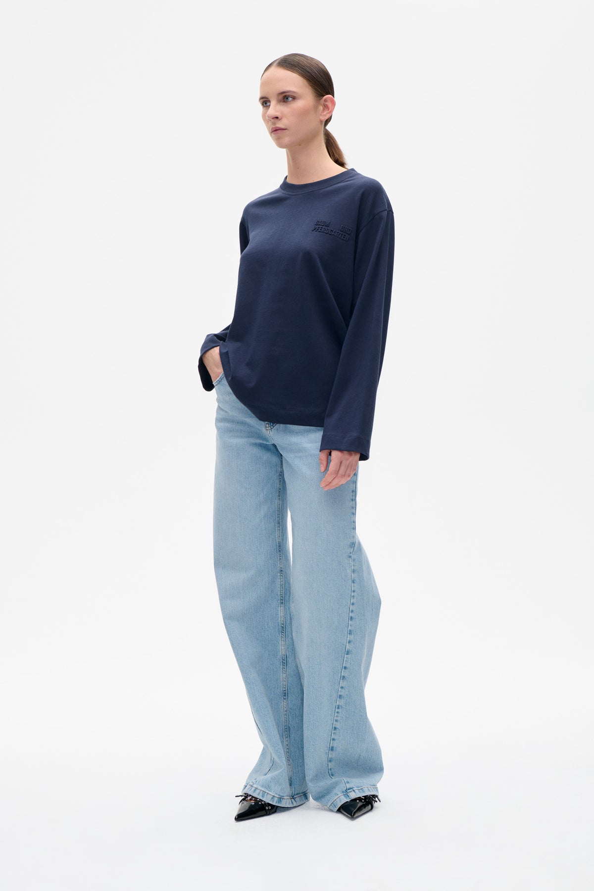 Front view of a model wearing a navy crew-neck sweatshirt with tonal chest lettering and light-wash wide-leg jeans.