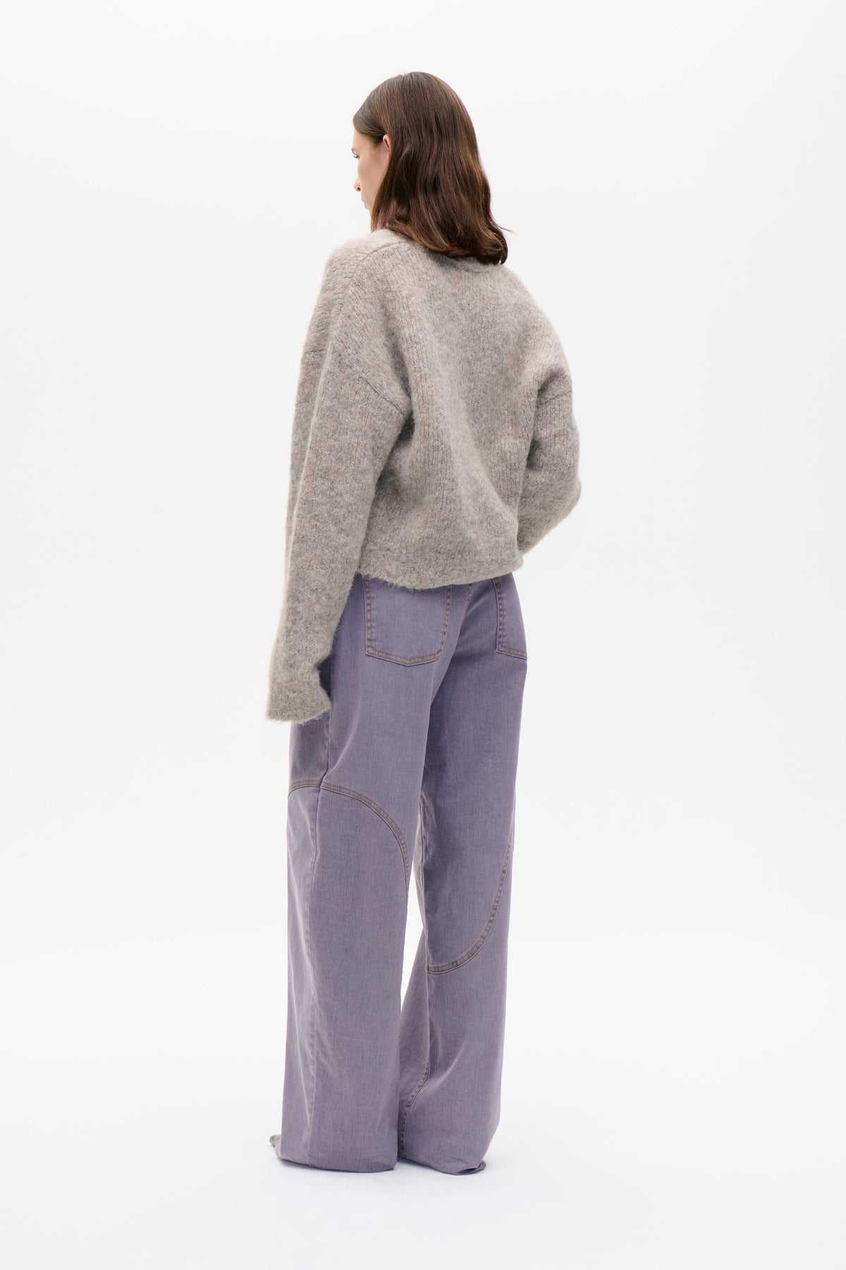 Model seen from behind wearing a loose, flecked taupe knit sweater and wide-leg lavender jeans.