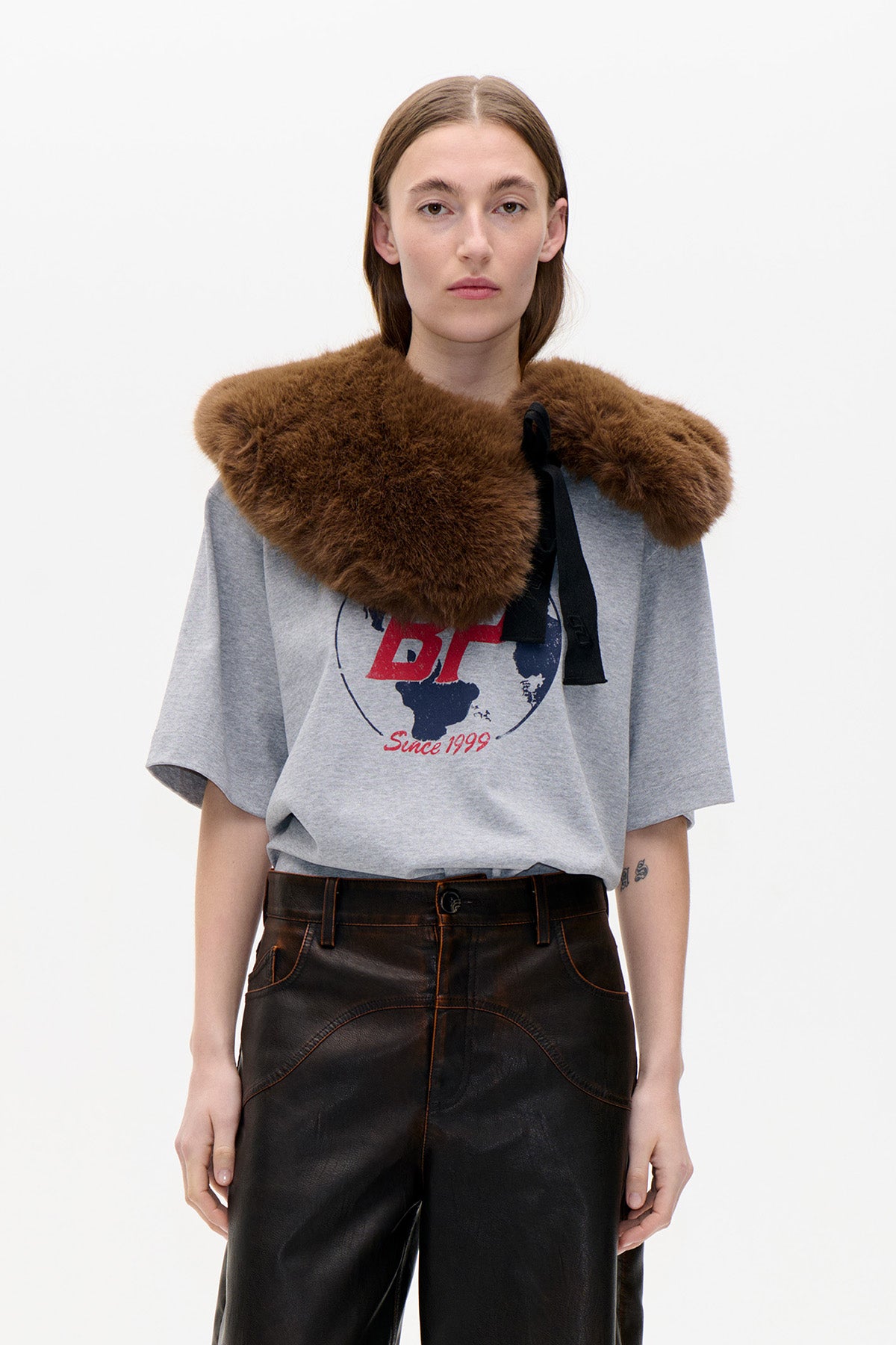 Model wearing a wide brown fluffy collar with a black ribbon over a grey graphic T-shirt and dark trousers