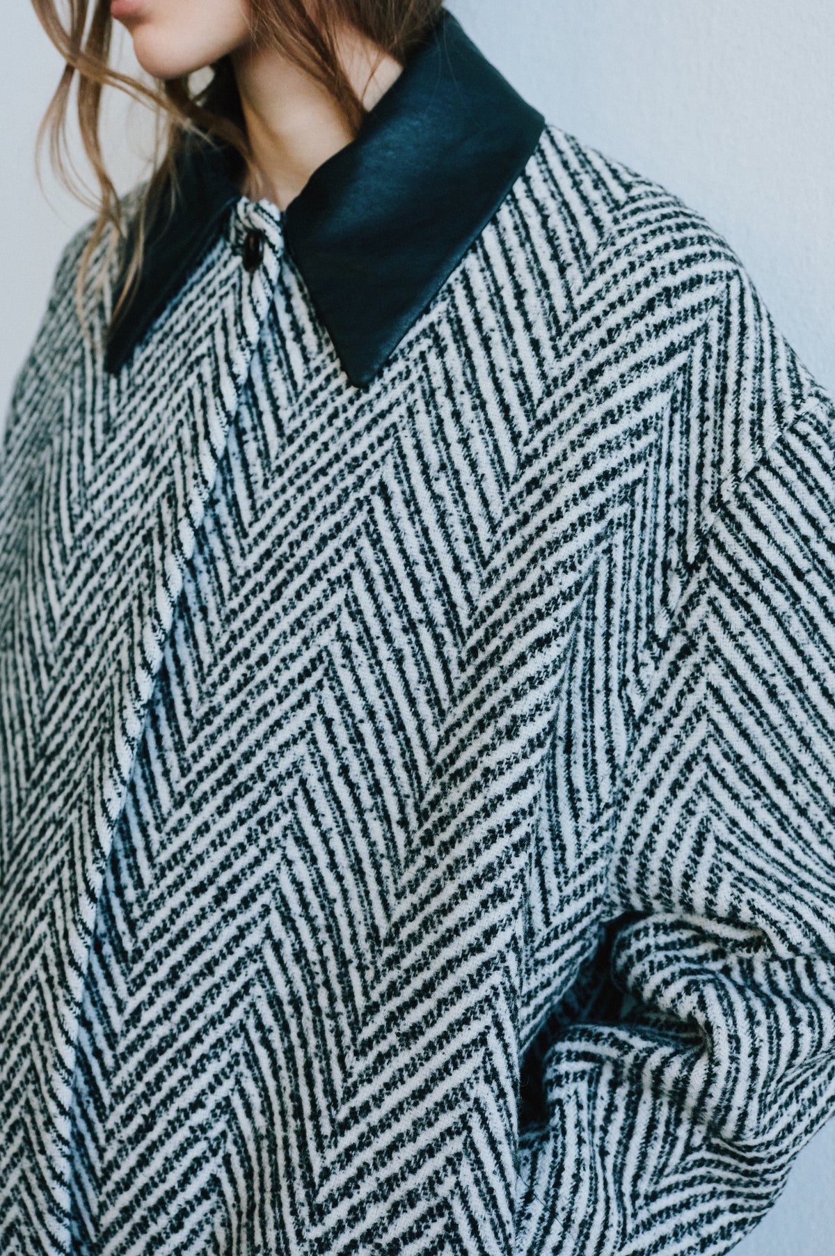 Close-up campaign portrait of a model wearing a black-and-cream geometric-patterned knit cardigan with a wide dark navy collar.