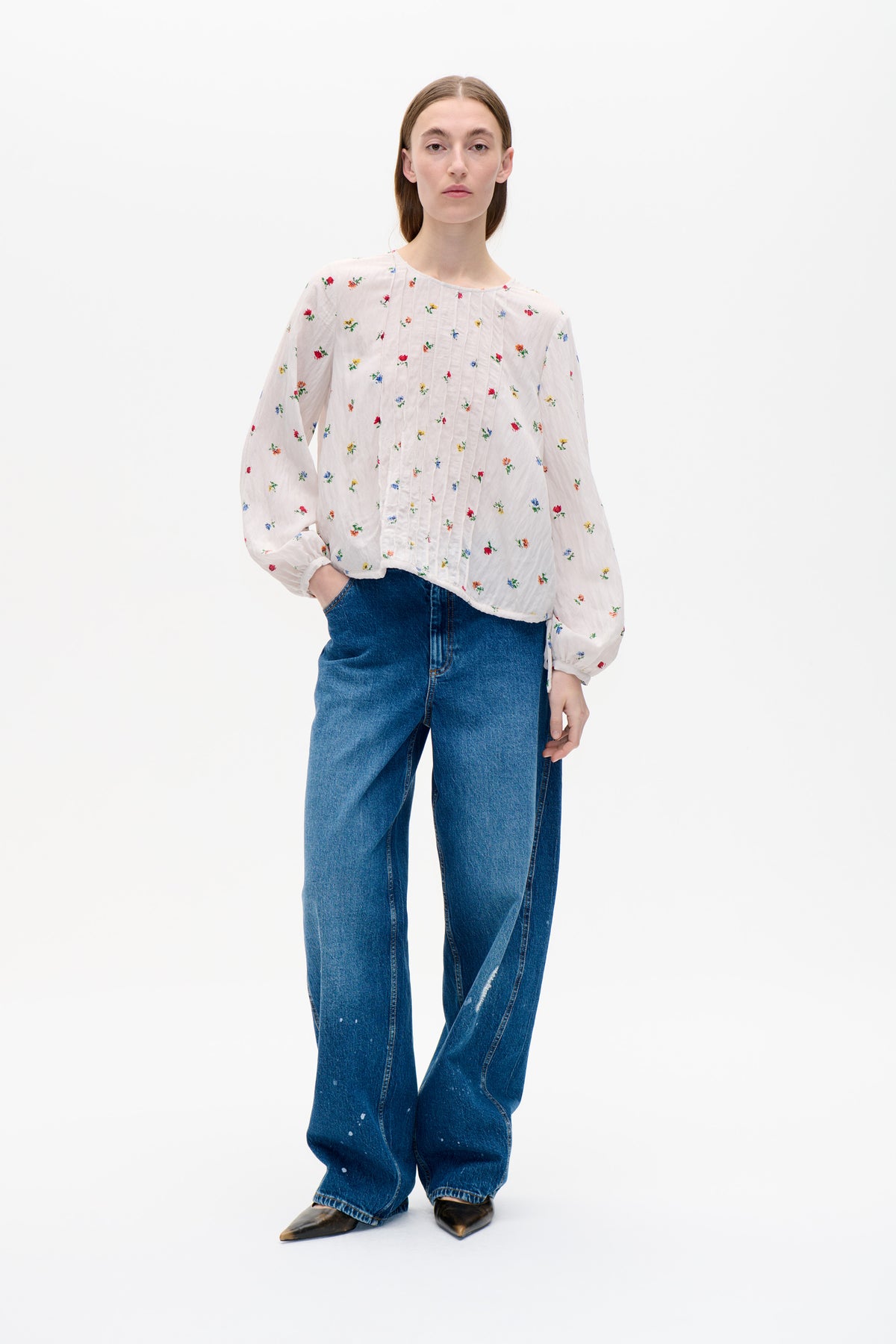 Model wearing a white blouse with scattered multicolour floral print, pintuck front and voluminous sleeves, paired with blue jeans.