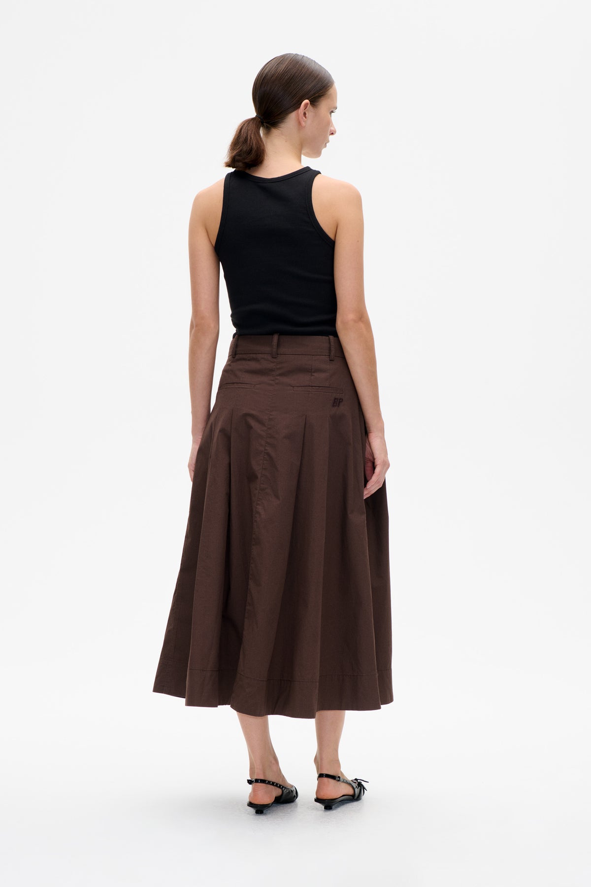 Back view of a model wearing a black sleeveless top and a dark brown flared midi skirt with belt loops and welt pockets.