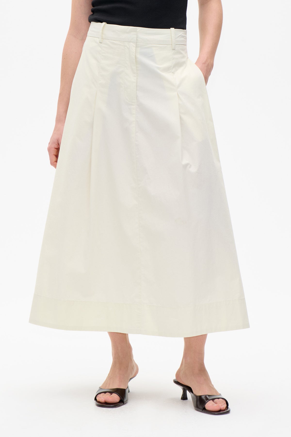 Front detail of an ivory A-line midi skirt with belt loops, side pockets and vertical panel seams, styled with a black top.