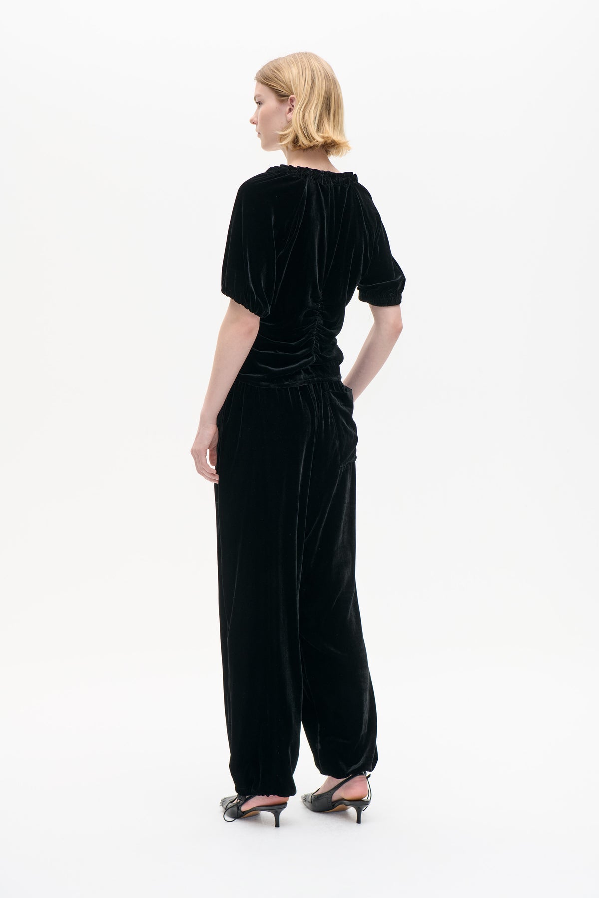 Model viewed from behind wearing a black velvet top with a gathered neckline and waist, and matching wide-leg trousers with elasticated cuffs.