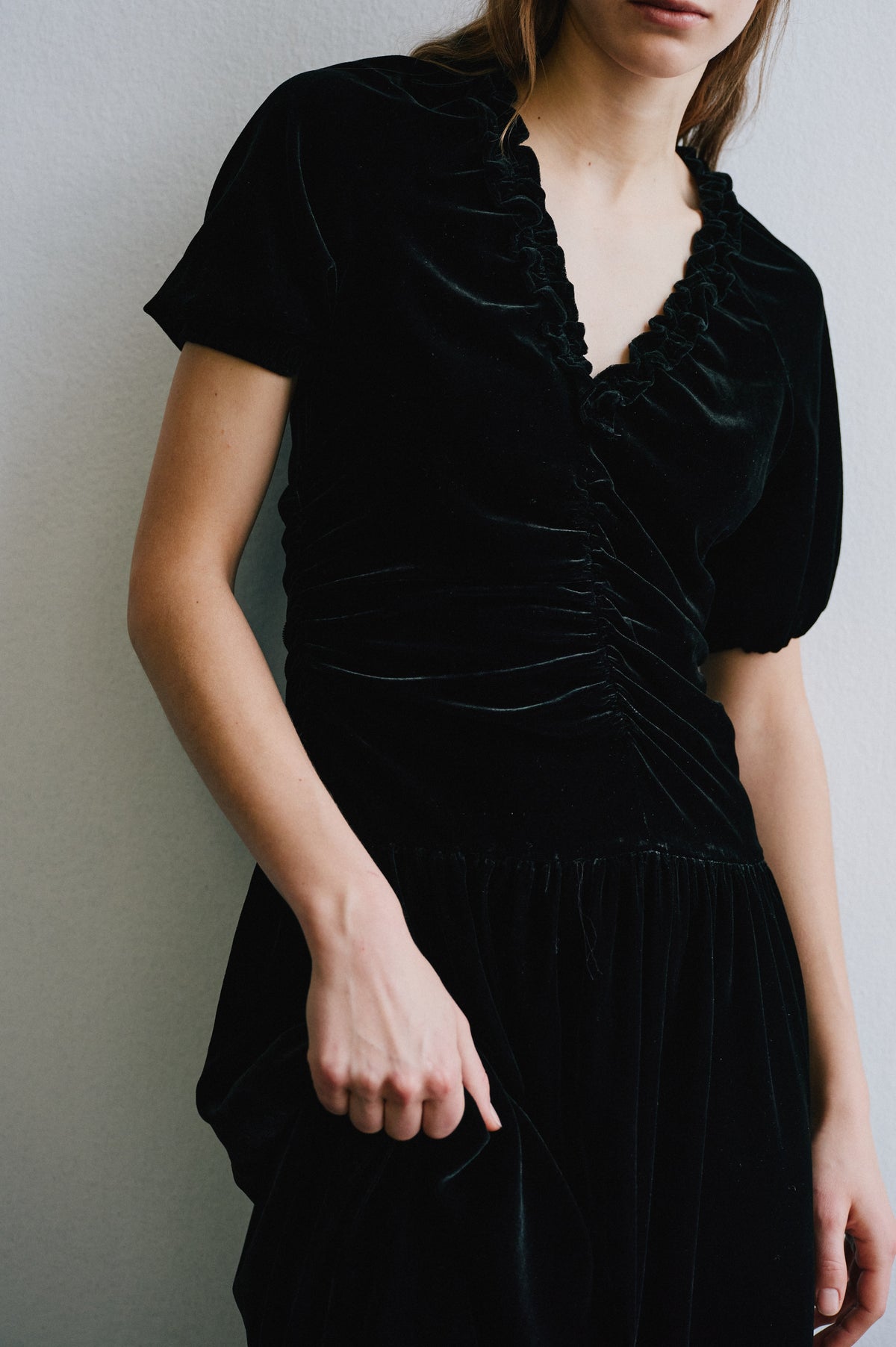 Close campaign view of a black velvet dress with short puff sleeves, a ruffled V-neckline, fitted waist and pleated skirt.