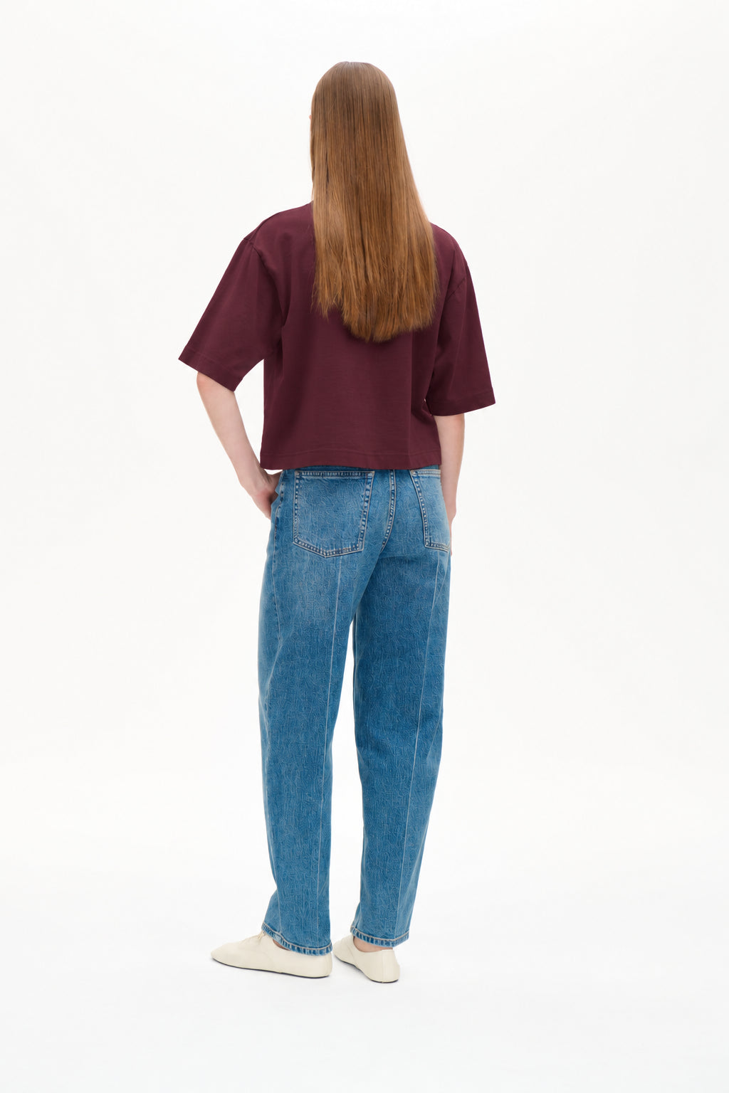 Achteraanzicht van een model in een bordeauxrode cropped T-shirt en een blauwe jeans met een subtiel tonale print en klepzakken.