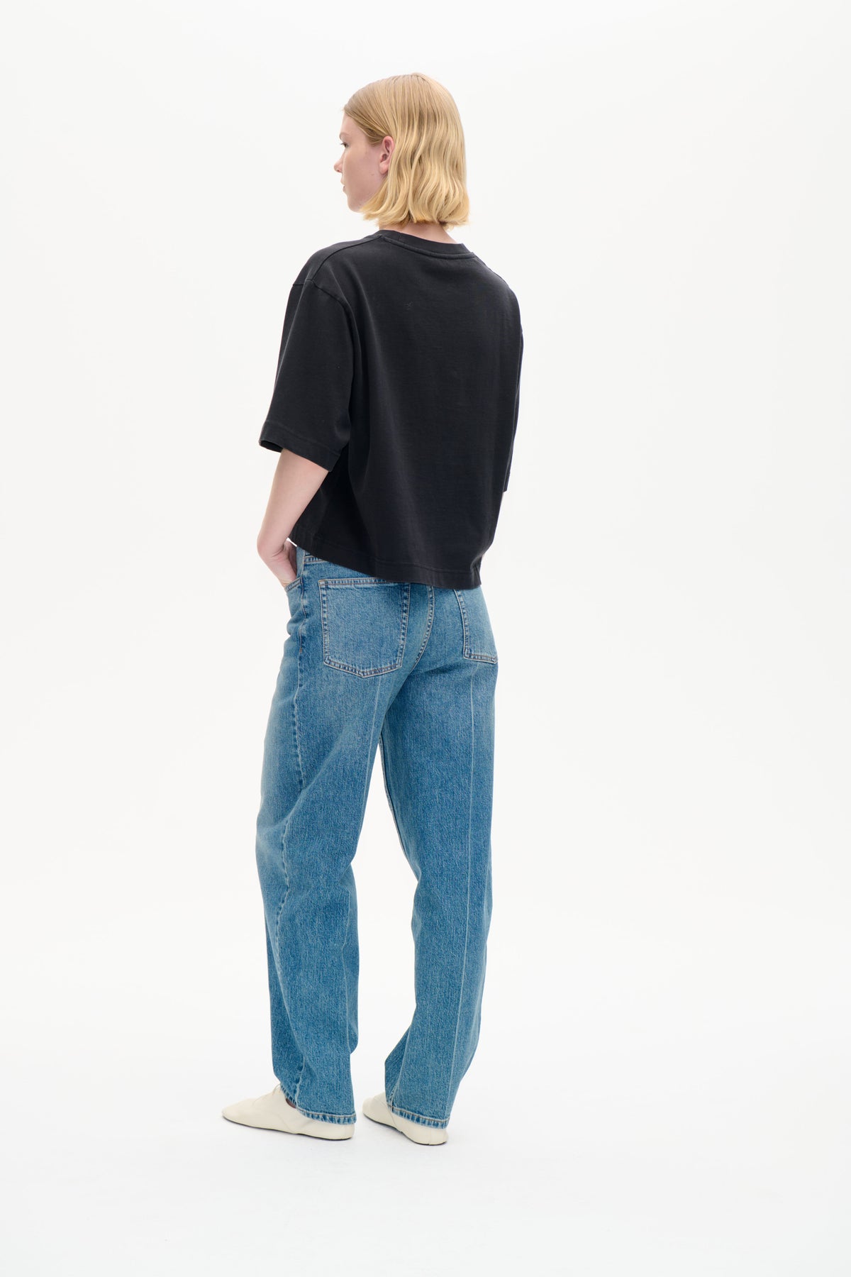 Rückenansicht eines Models, das ein oversized anthrazitfarbenes Kurzarm-T-Shirt mit einem kleinen, dezenten Fleck sowie blaue Jeans trägt.