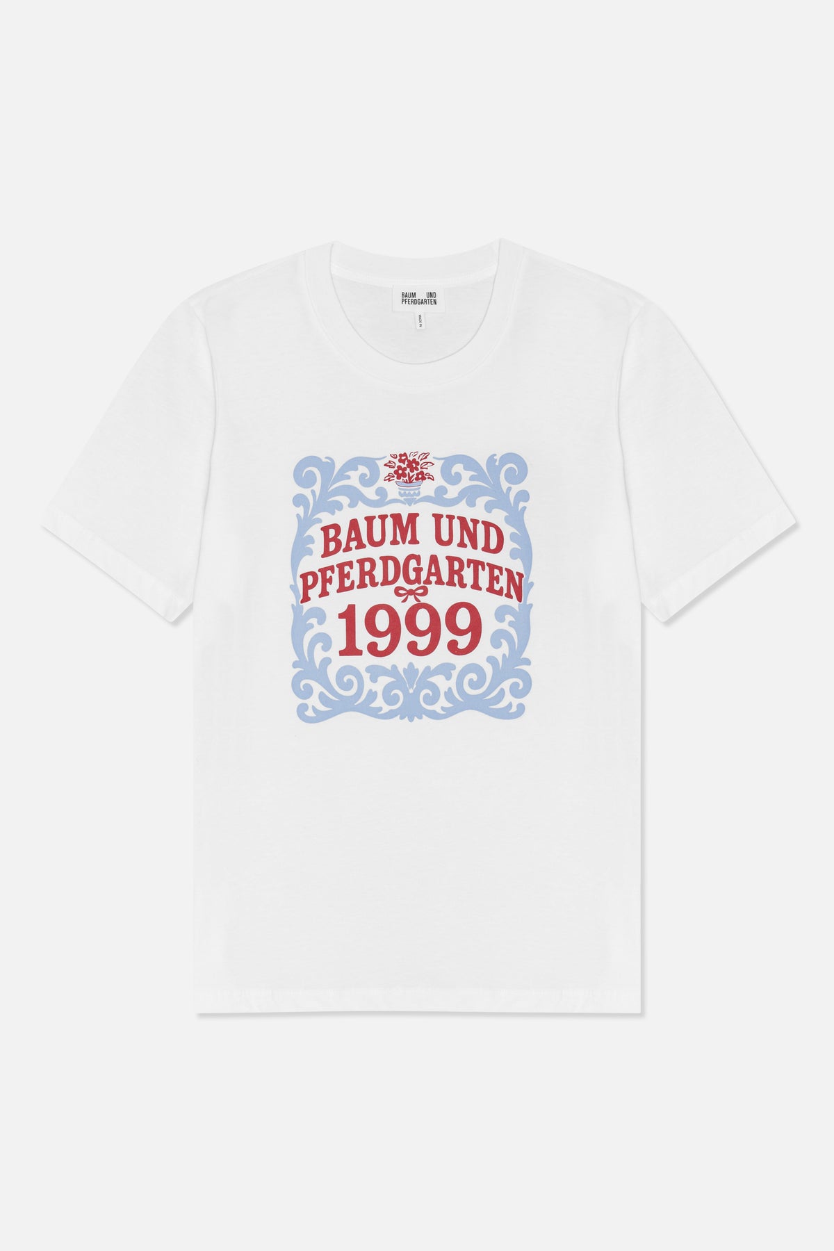 Front view of a white short-sleeved T-shirt with a blue ornamental frame, red floral detail and “Baum und Pferdgarten 1999” text.