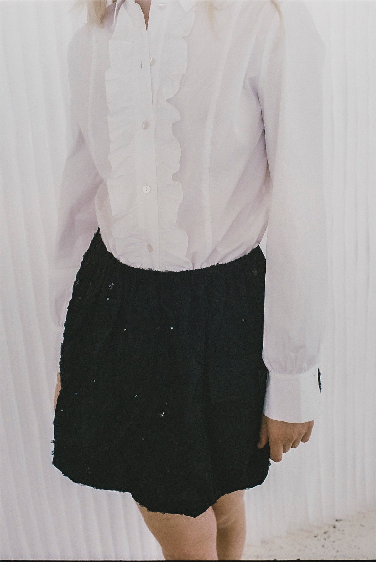 Close-up campaign view of a model in a white ruffled button-front blouse and a black skirt with scattered sequins.