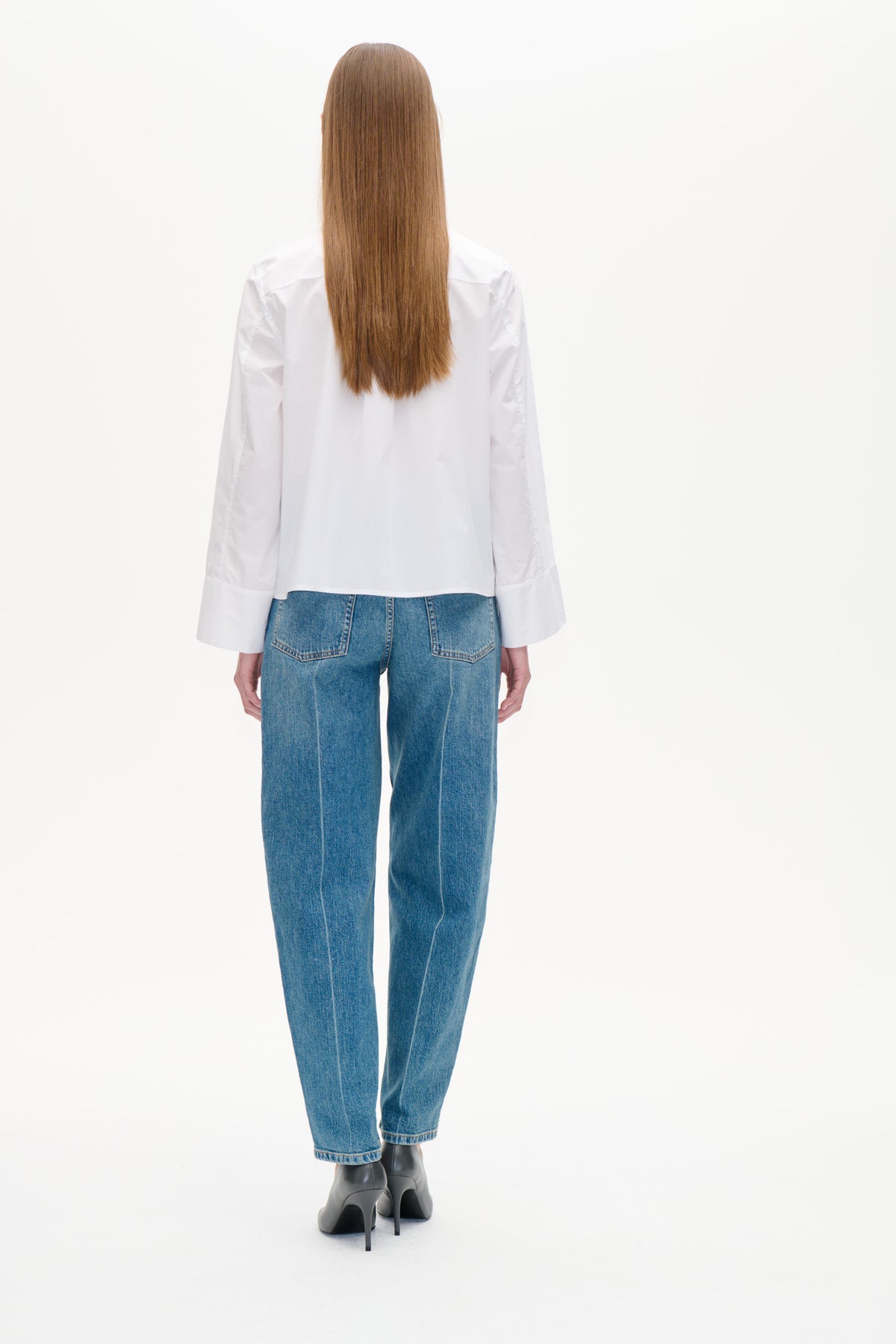 Vue de dos d'un mannequin portant une blouse blanche à manches longues et poignets larges, associée à un jean bleu à poches plaquées au dos.