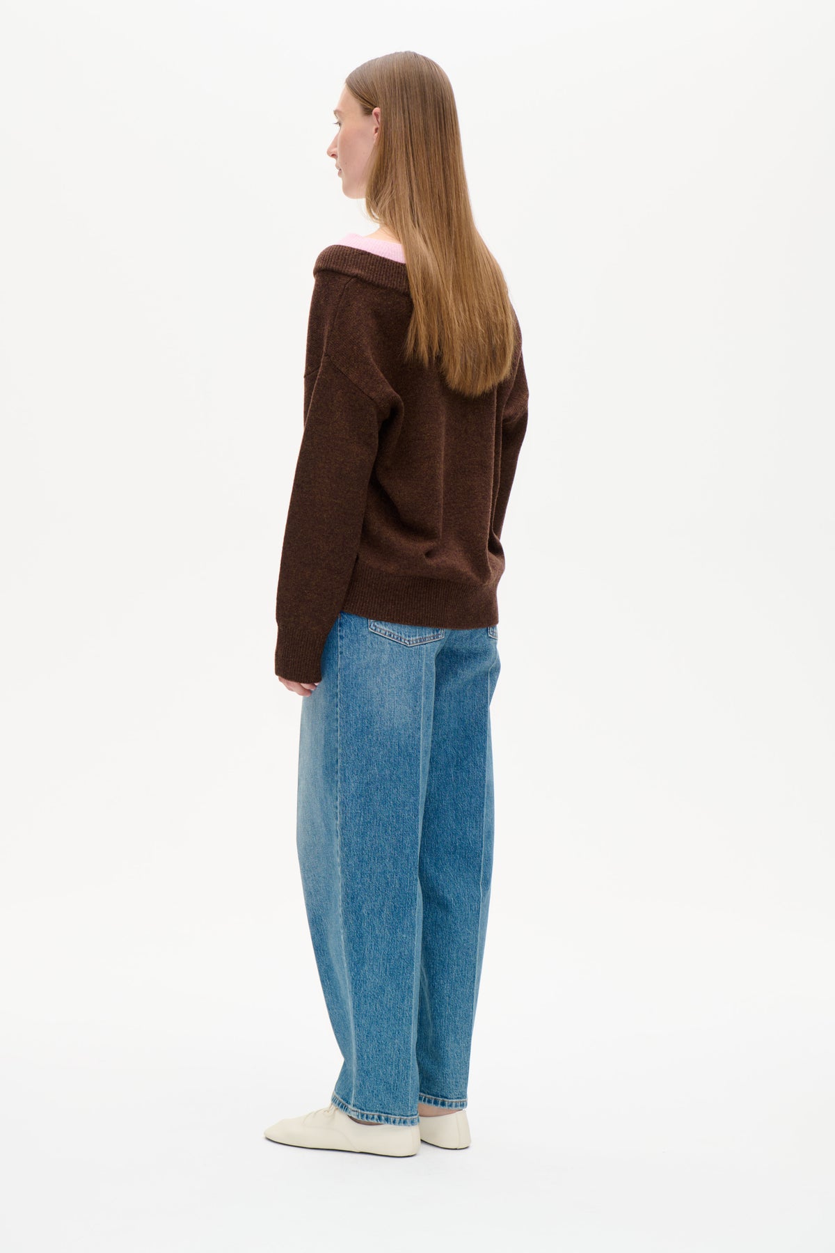 Back view of a model wearing a dark brown knit sweater with a wide folded neckline revealing a pale pink layer.