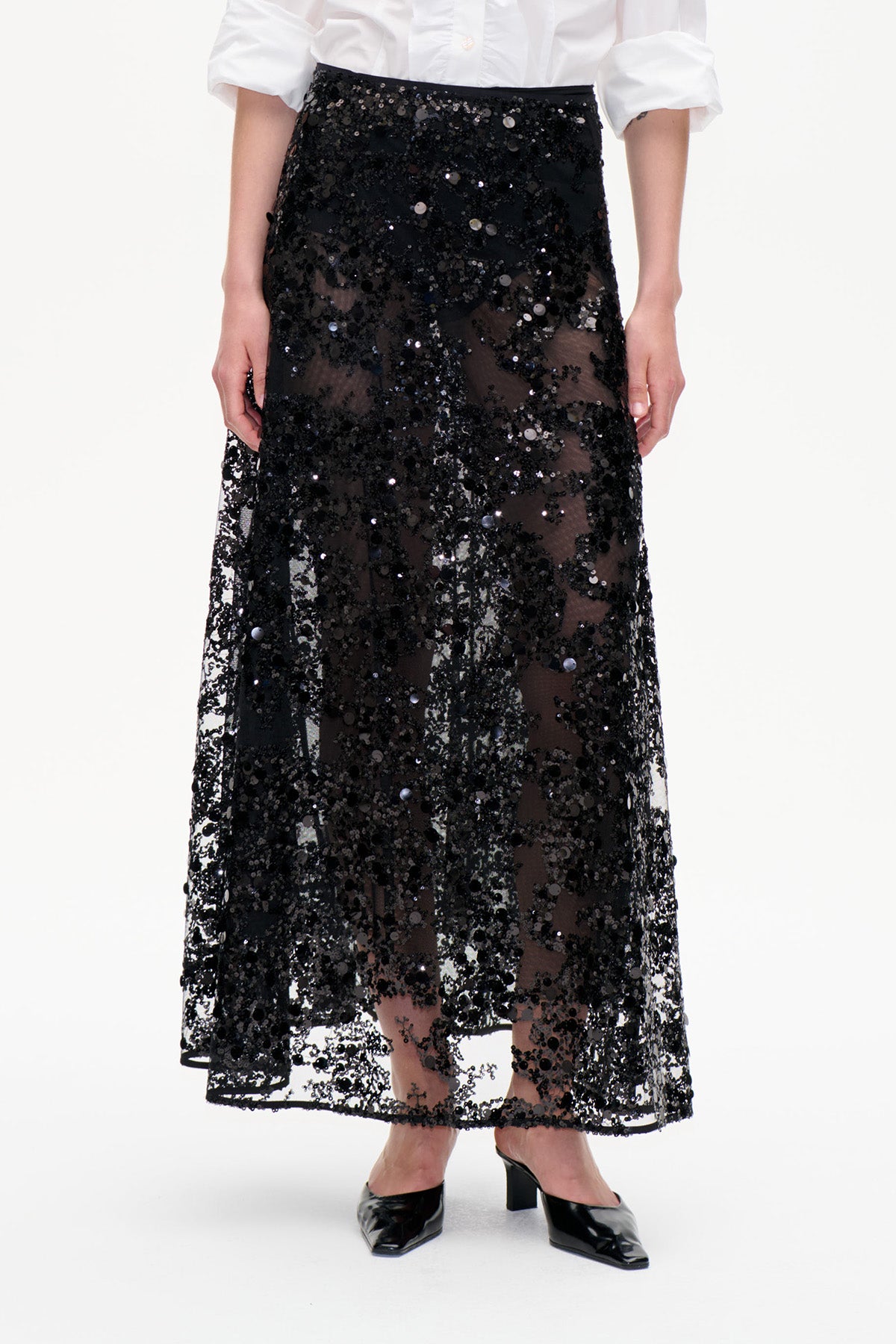 Front view of a sheer black ankle-length skirt covered in scattered sequins, worn with a white shirt.