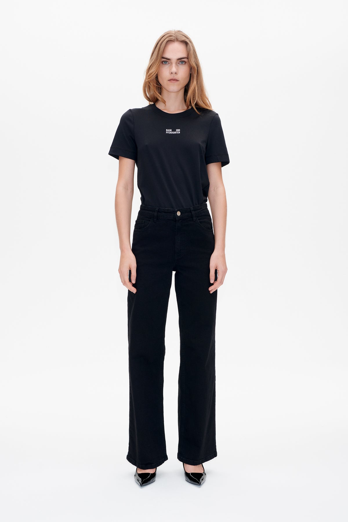 Front view of a model wearing a black short-sleeved T-shirt with a small white chest logo and black wide-leg jeans.