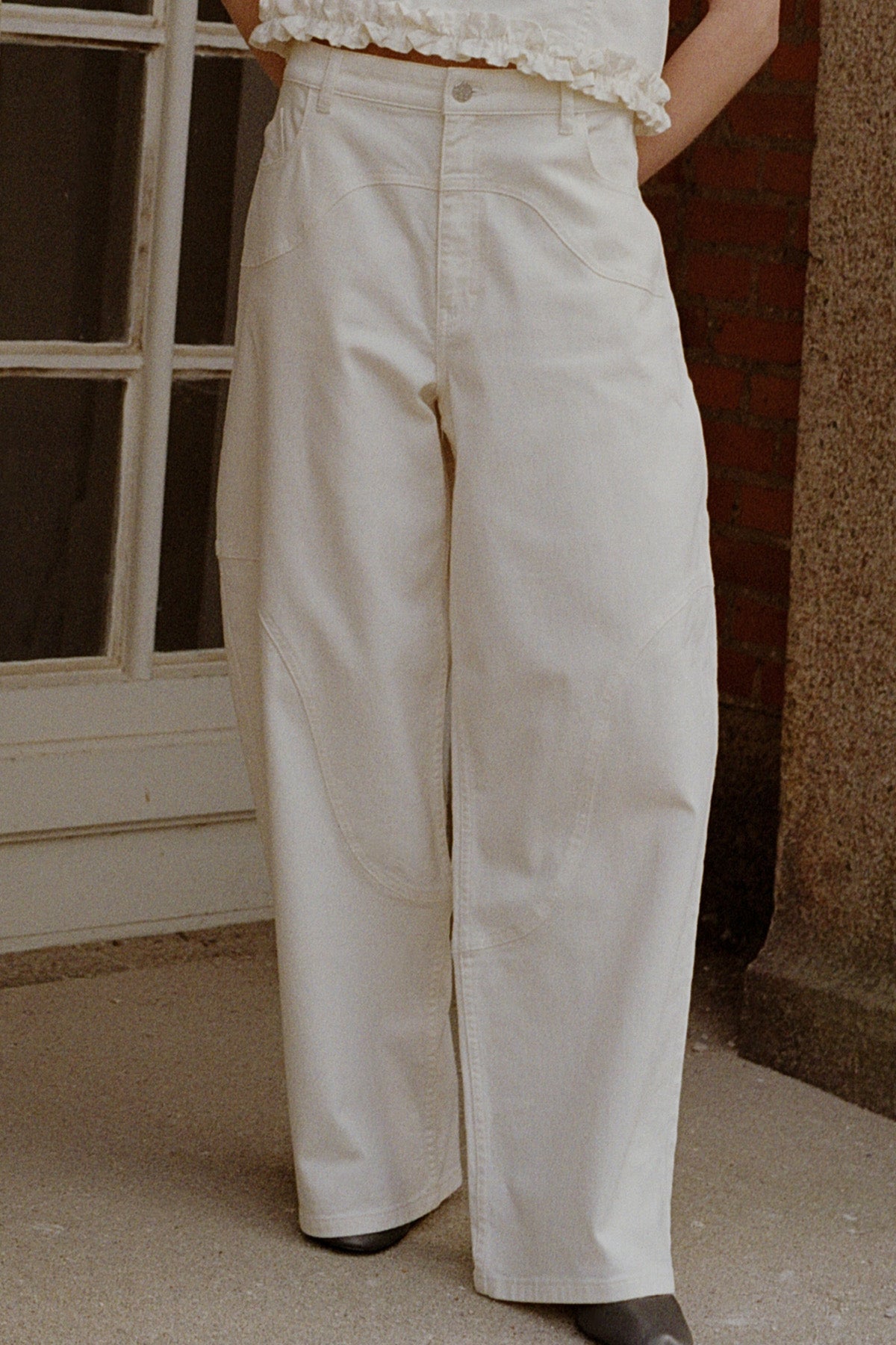 Front detail of off-white wide-leg trousers with curved patch pockets, worn with a white ruffled top.