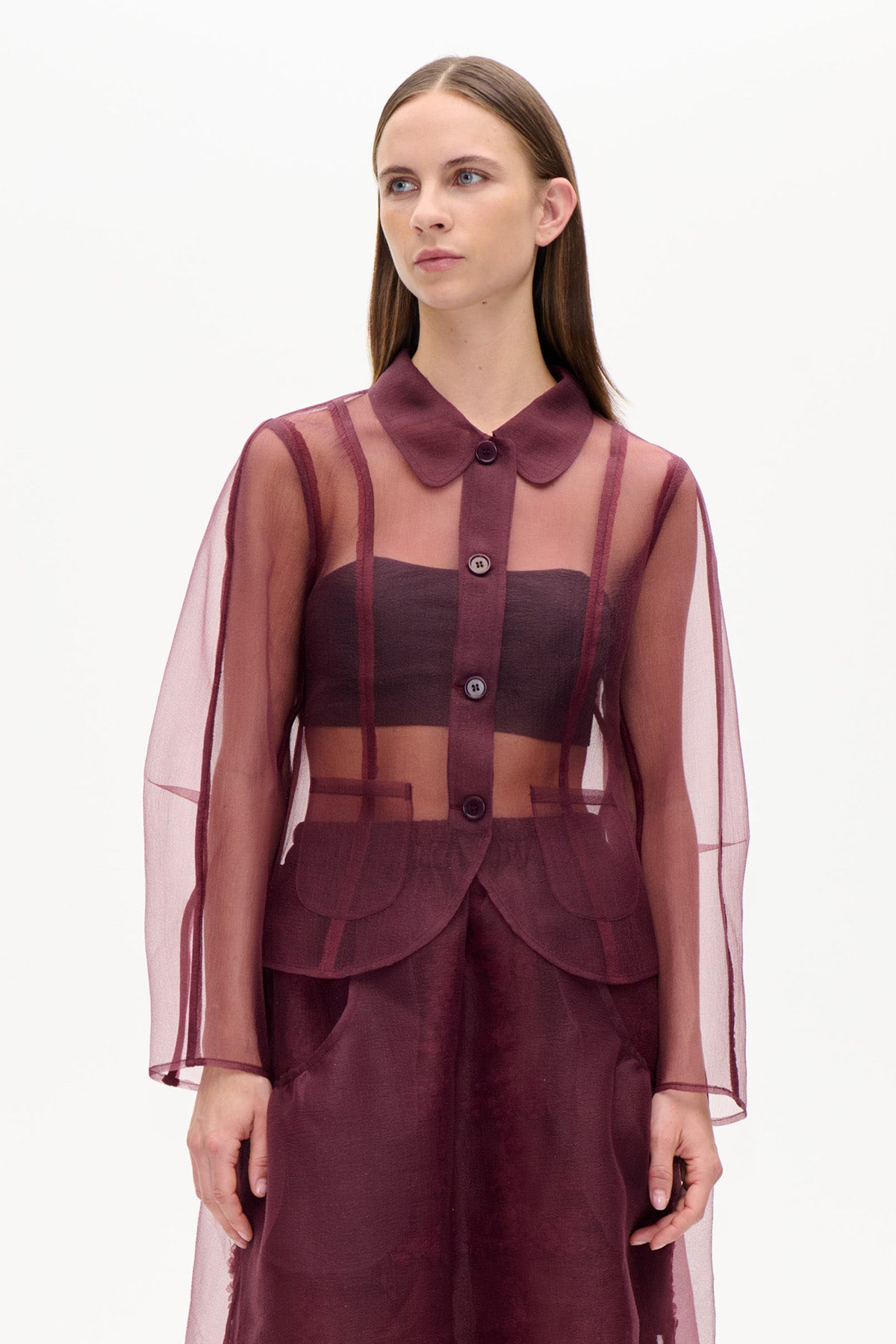 Front view of a sheer burgundy button-front blouse with a rounded collar and wide sleeves, layered over a dark bandeau top and matching trousers.