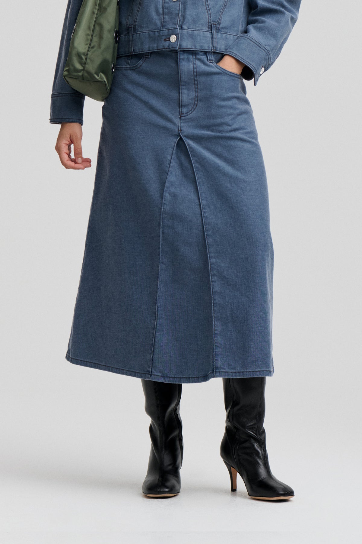 Nahaufnahme von vorn eines Models, das eine blaue denim-Jacke und einen passenden langen Rock mit Teilungsnähten und einem vorderen Schlitz trägt.