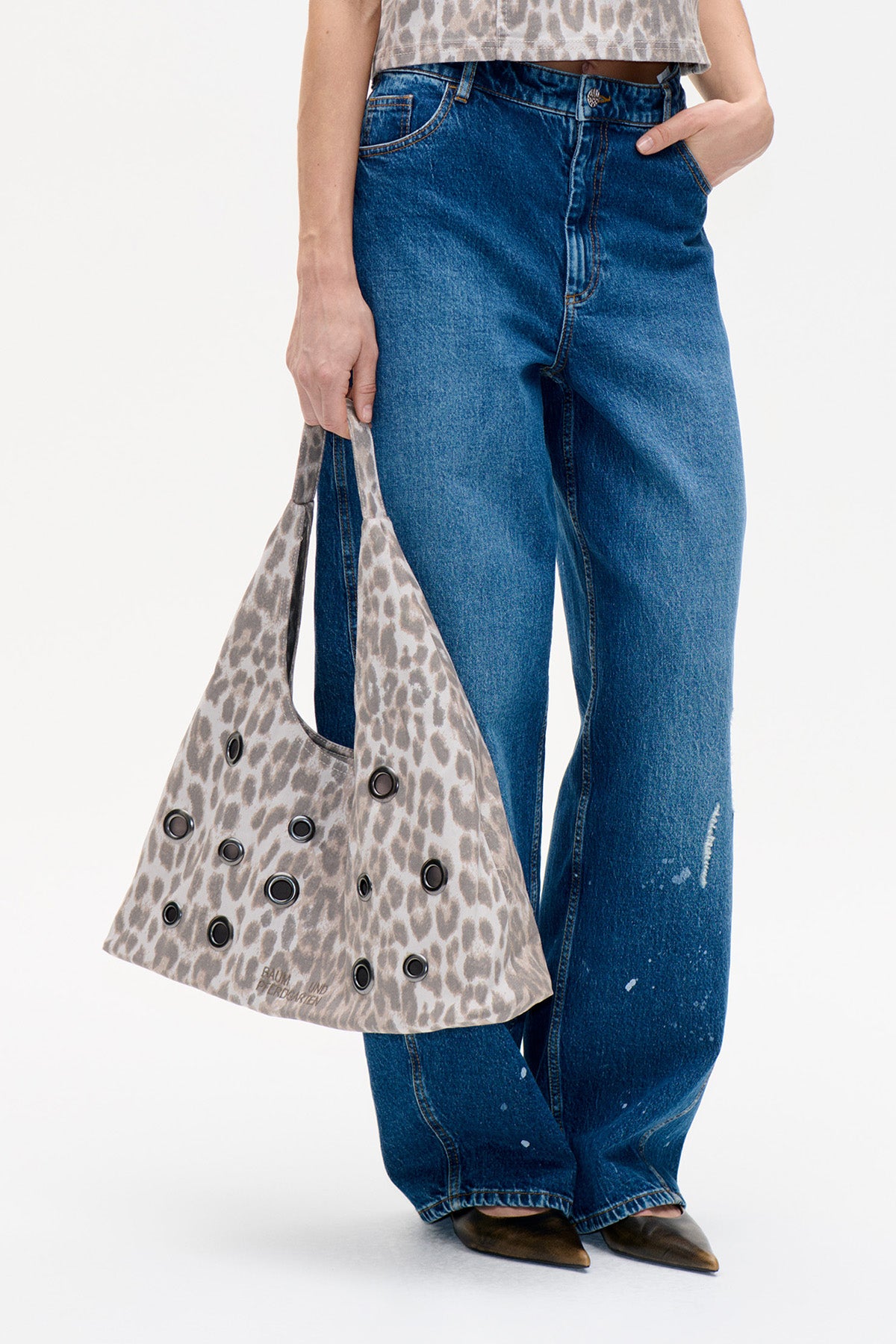 Leopard-print tote bag with black metal eyelets, carried beside blue jeans in a close-up styling view.