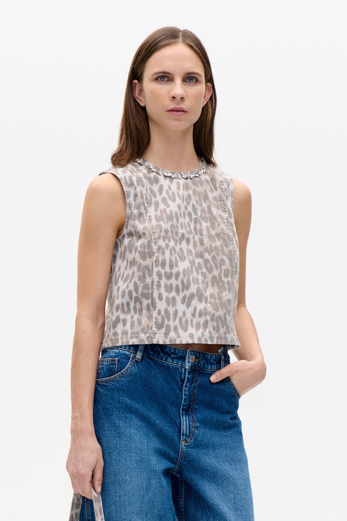 Model wearing a sleeveless beige and grey animal-print top with a silver embellished neckline and blue jeans.