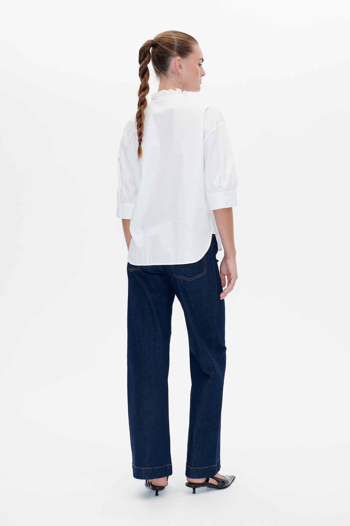Rückenansicht einer weißen Bluse mit Rüschenkragen und ellenbogenlangen Ärmeln, kombiniert mit Jeans mit weitem Bein in dunklem Indigo.