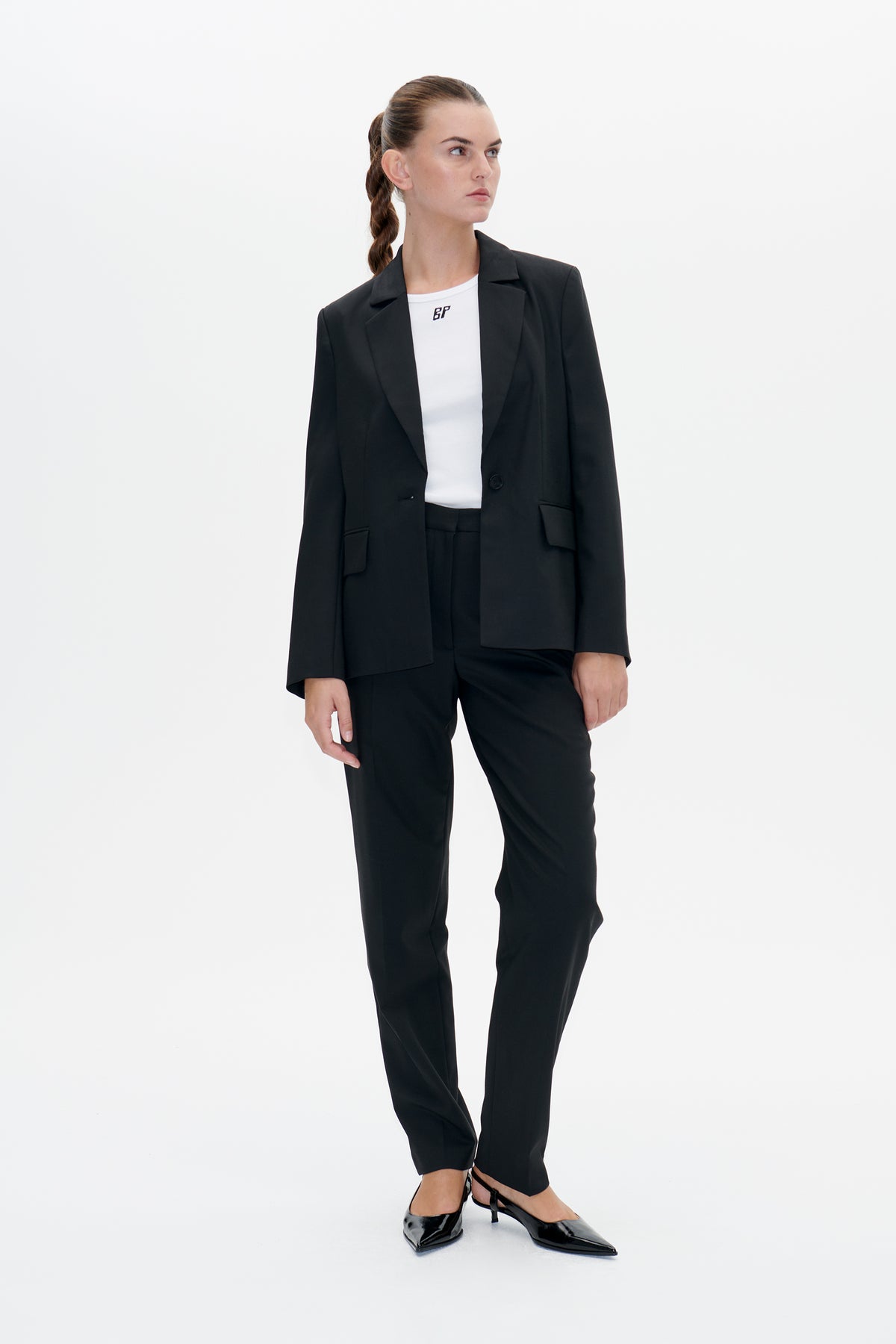 Model wearing a black notched-lapel blazer and trousers with a white logo T-shirt, shown from the front against a plain background.