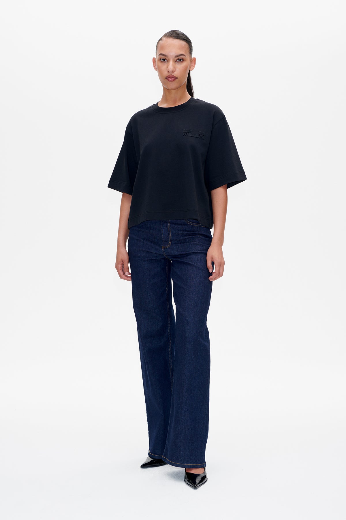 Model wearing a black oversized short-sleeve T-shirt with a small chest logo and dark blue wide-leg jeans, front view.