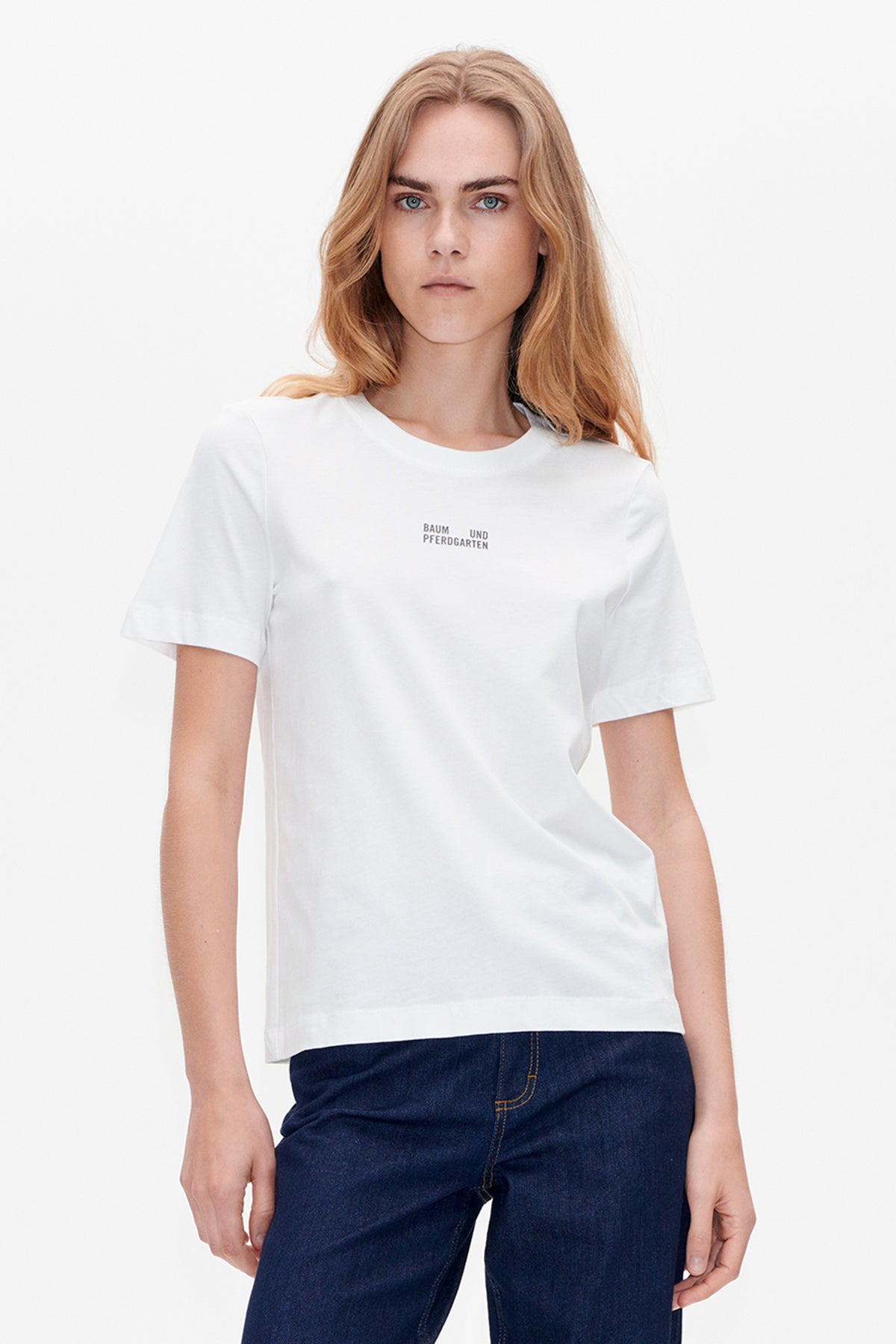 Vorderansicht eines weißen Kurzarm-T-Shirts mit kleinem Baum und Pferdgarten-Logo, kombiniert mit dunkelindigo-Jeans.