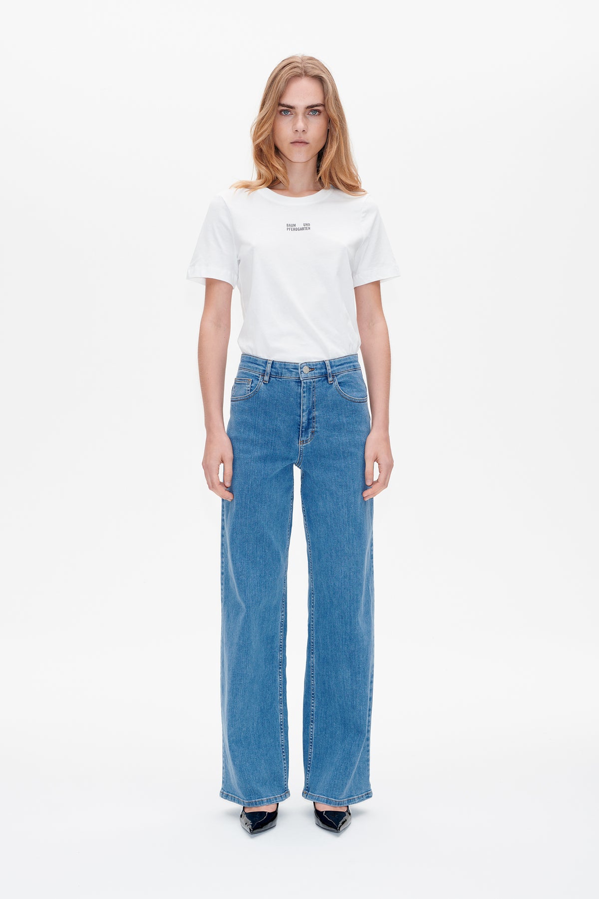 Front view of a white short-sleeved T-shirt with a small Baum und Pferdgarten chest print, paired with blue wide-leg jeans.