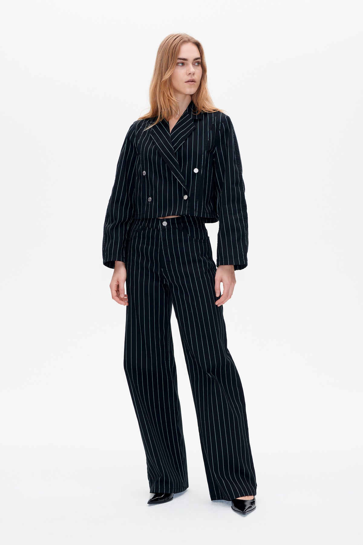 Front view of a model wearing a black pinstripe cropped double-breasted blazer with matching wide-leg trousers.