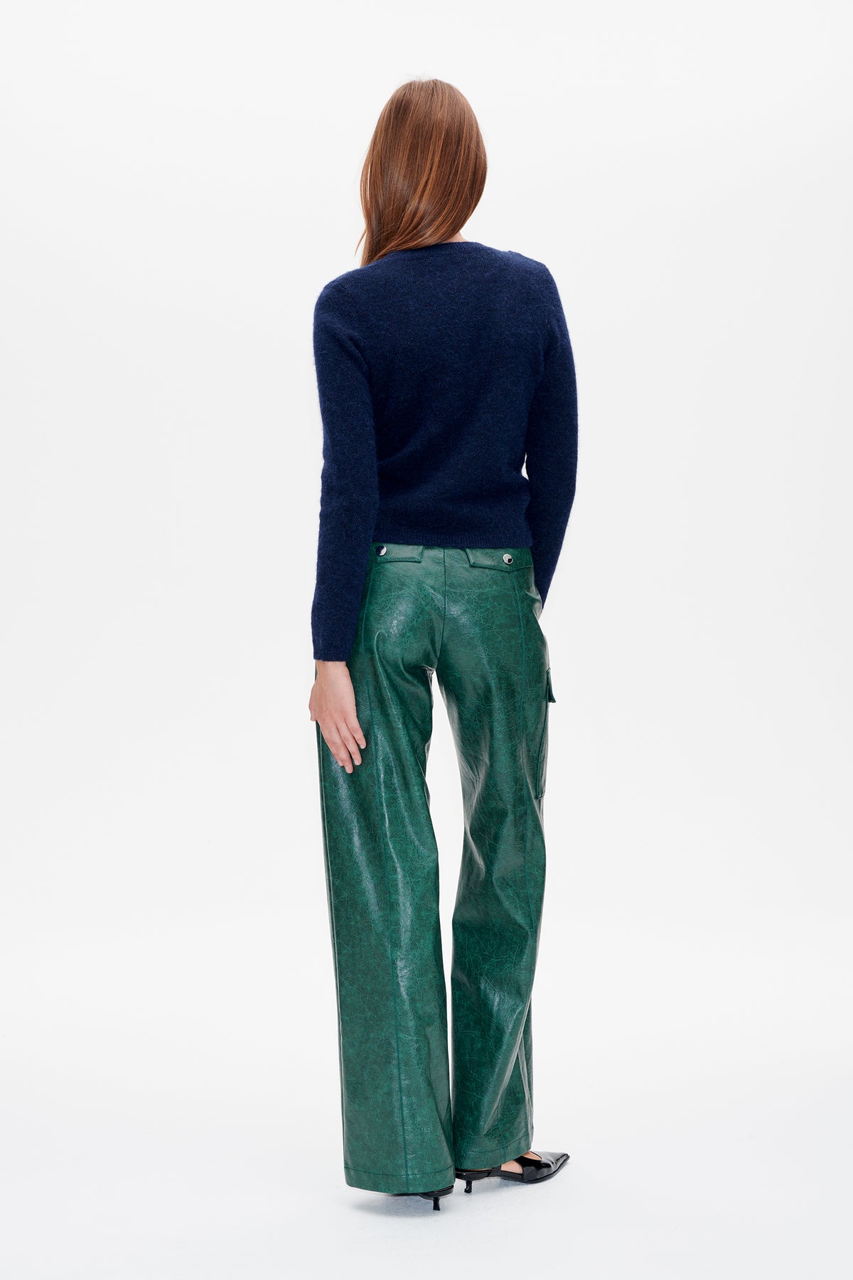 Back view of a model wearing a navy long-sleeved knit sweater with green, glossy wide-leg trousers.
