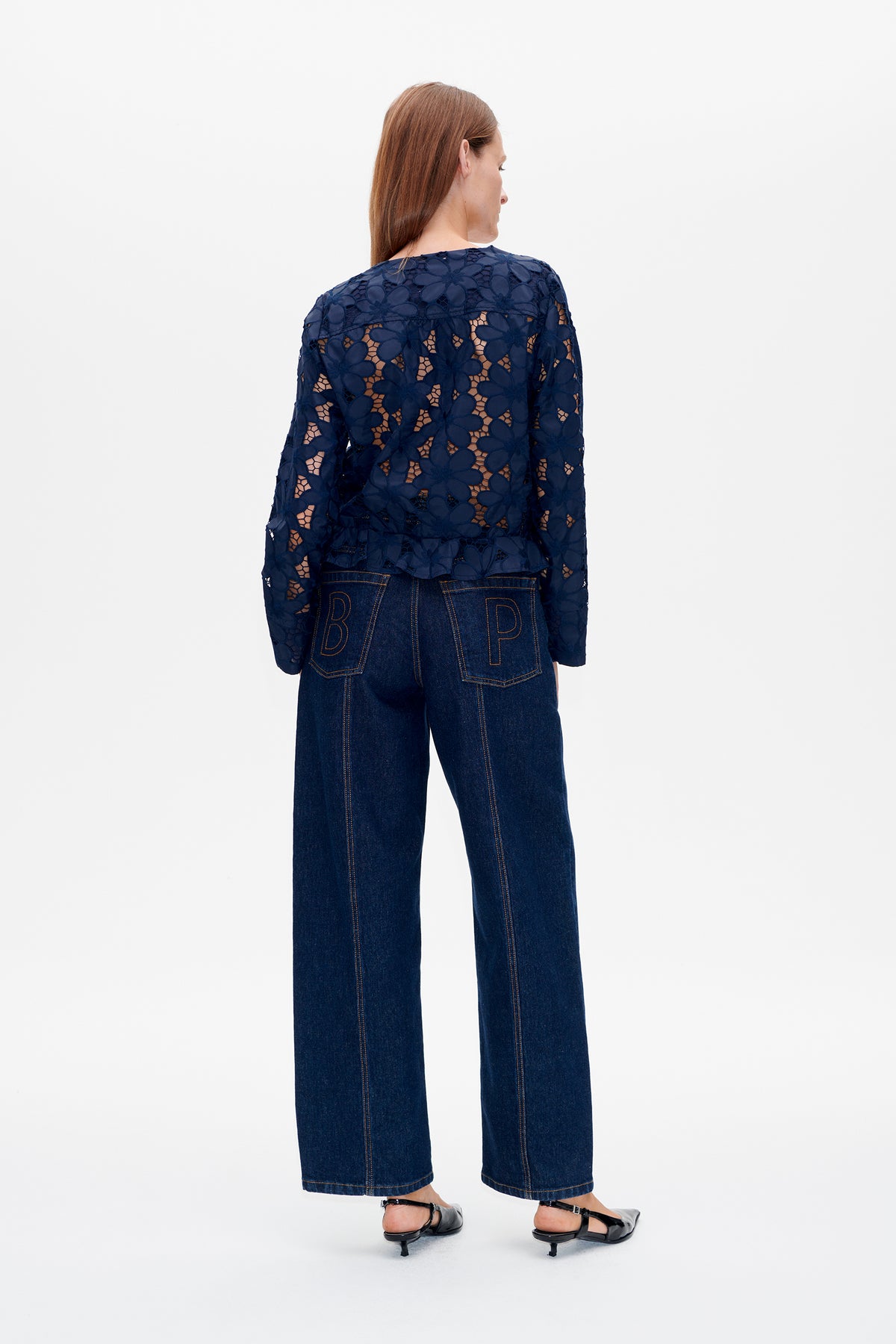 Back view of a model wearing a navy floral lace jacket with a peplum hem and dark wide-leg jeans.