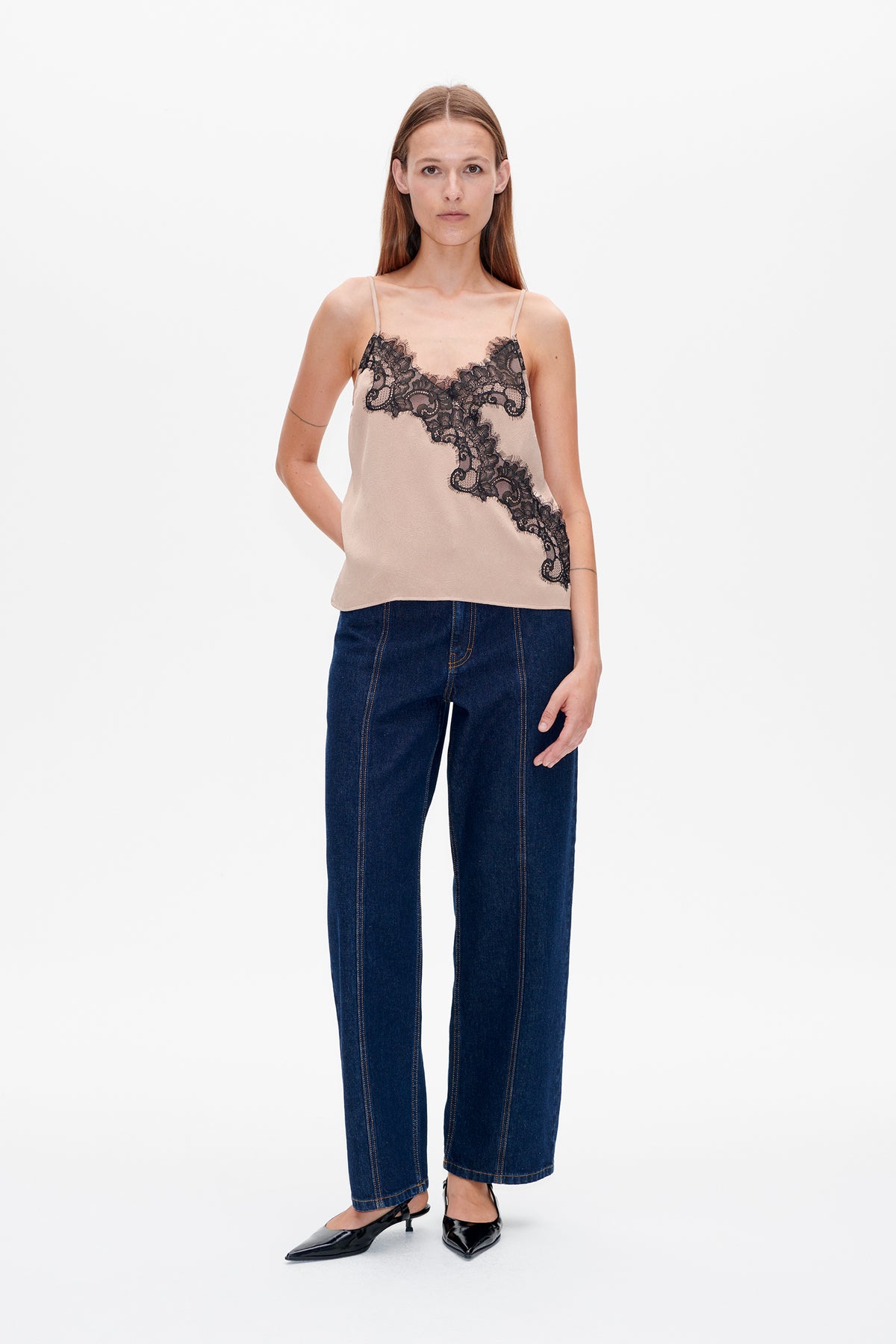 Vorderansicht eines Models, das ein hellrosa Trägertop mit schwarzem Spitzenbesatz und eine dunkelblaue Jeans trägt.