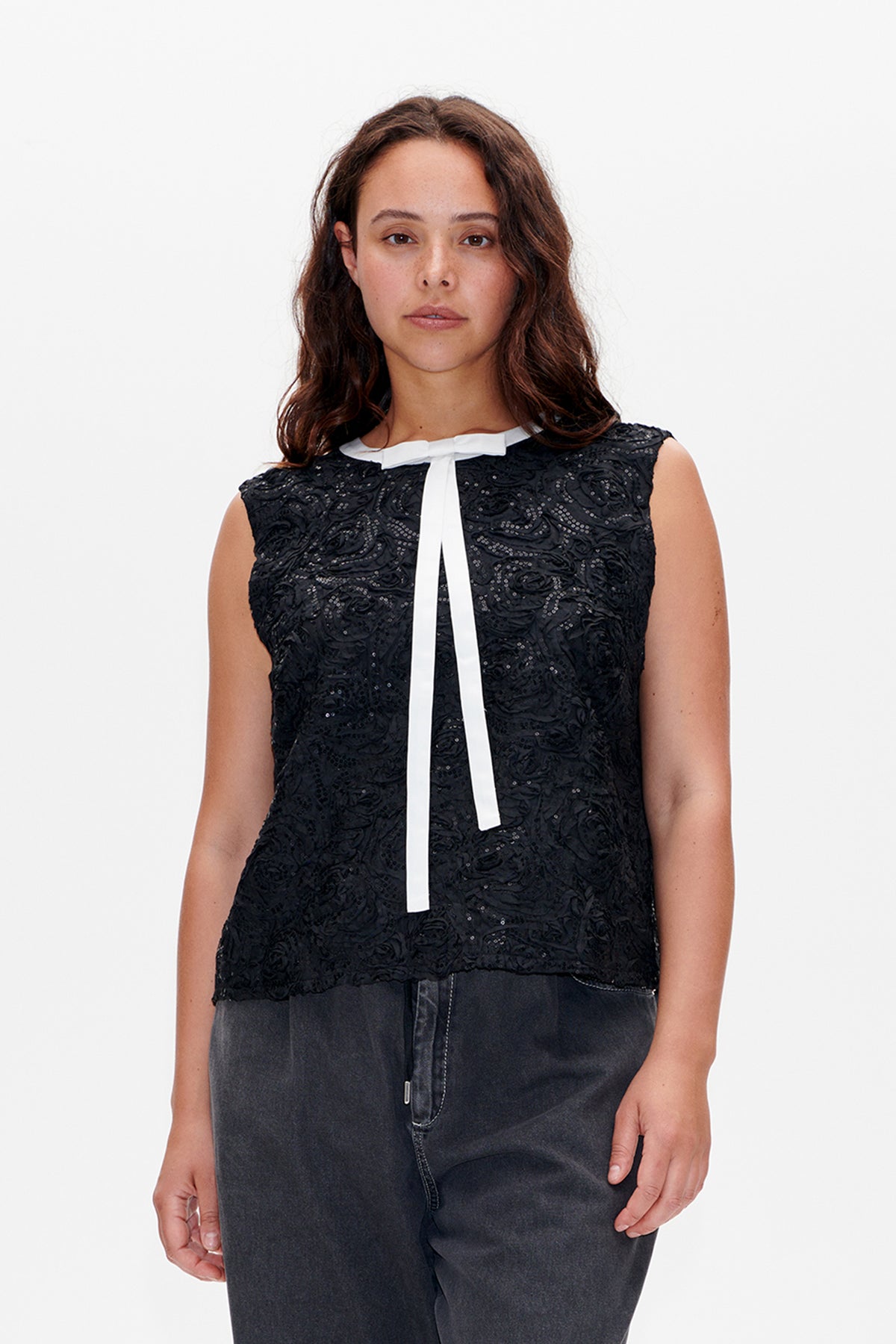 Front view of a black sleeveless top with raised floral texture and sequin details, finished with a long white neck tie.