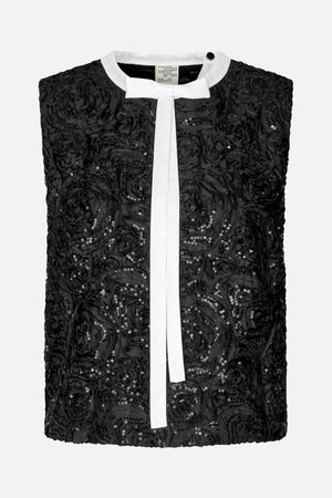 Front view of a black sleeveless top with raised floral detailing, scattered sequins, a white round collar and a long white bow tie.