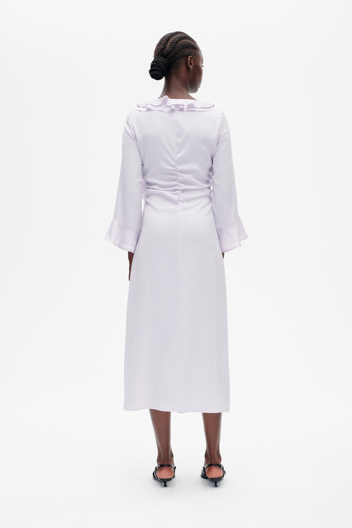 Back view of a pale lavender midi dress with a ruffled neckline, flared cuffs, ruched waist and subtle textured pattern.