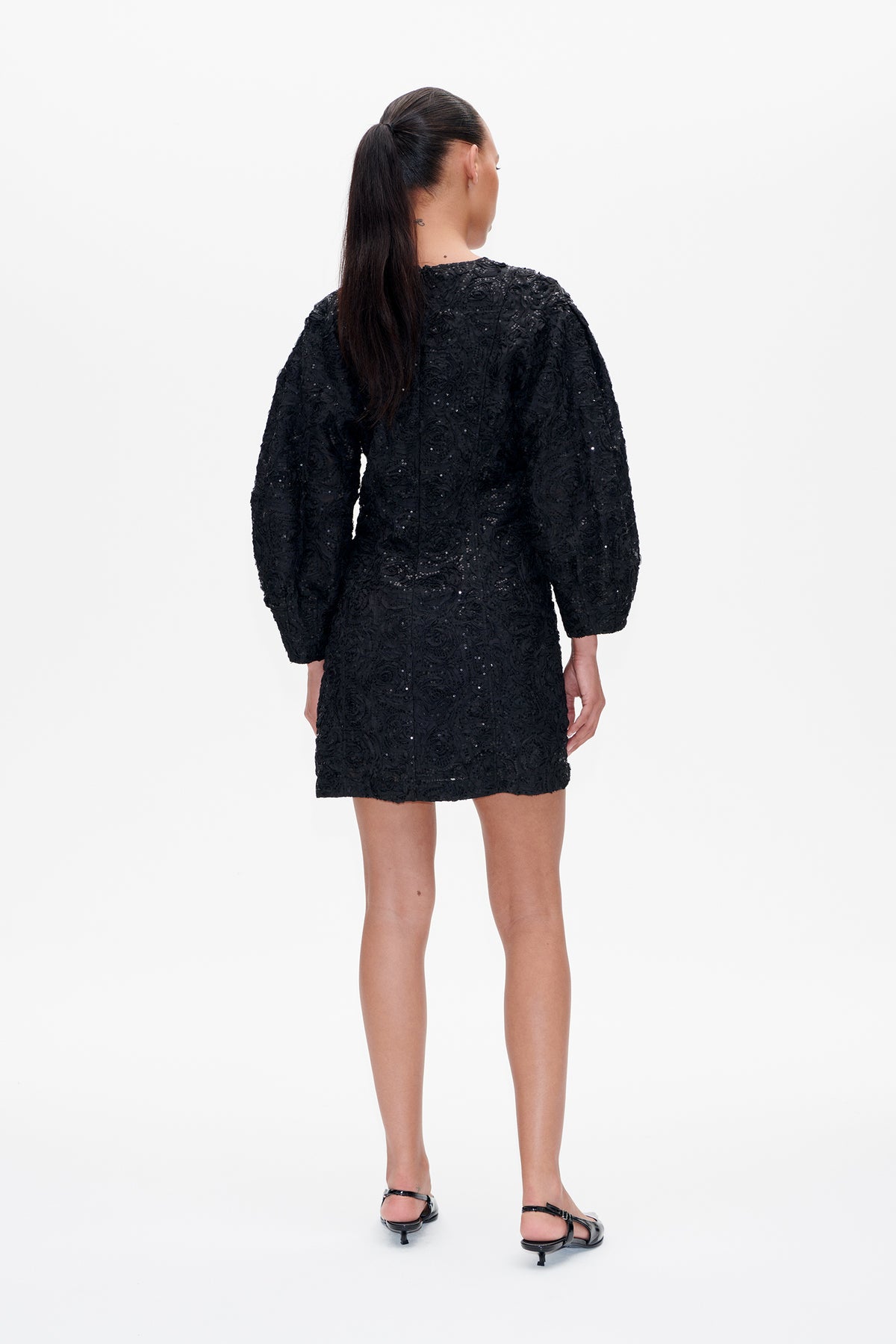 Back view of a black mini dress with long puff sleeves, textured swirling embellishments and subtle sequins.