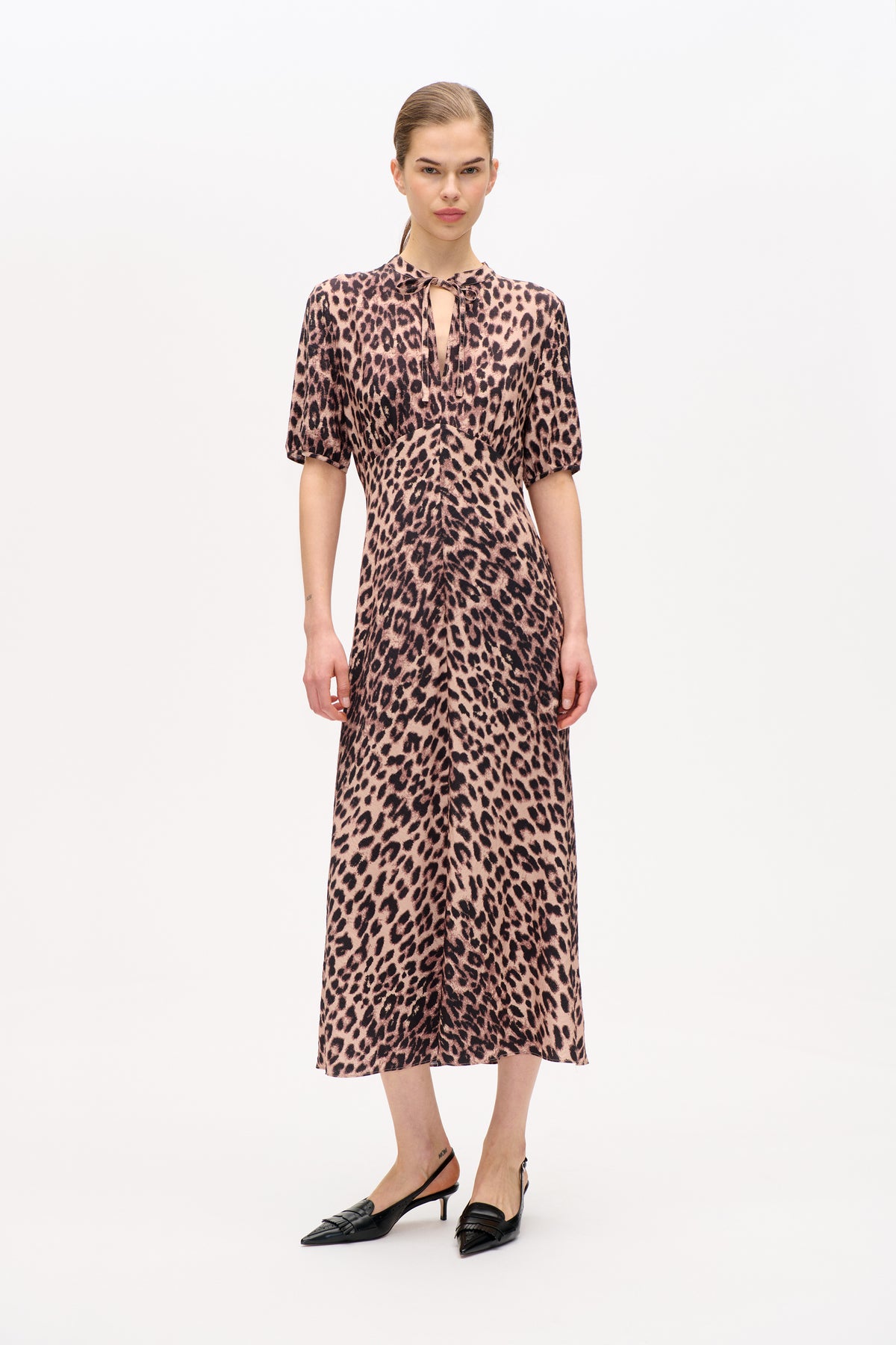 Front view of a model wearing a pink and black leopard-print dress with short sleeves and a tie neckline, paired with black heels.