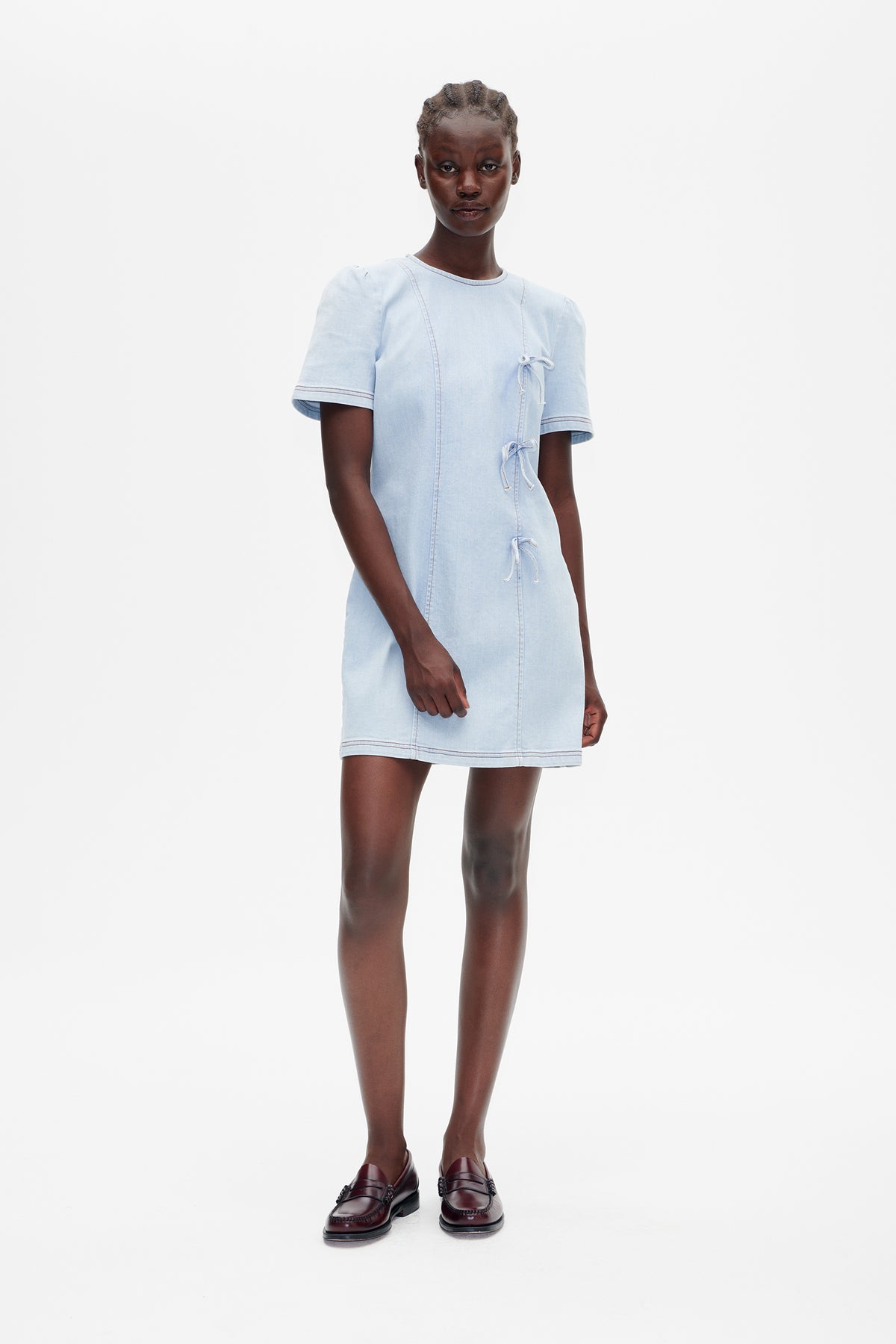 Model wearing a light blue short-sleeved mini dress with contrast stitching and three side-front tie closures, shown from the front.