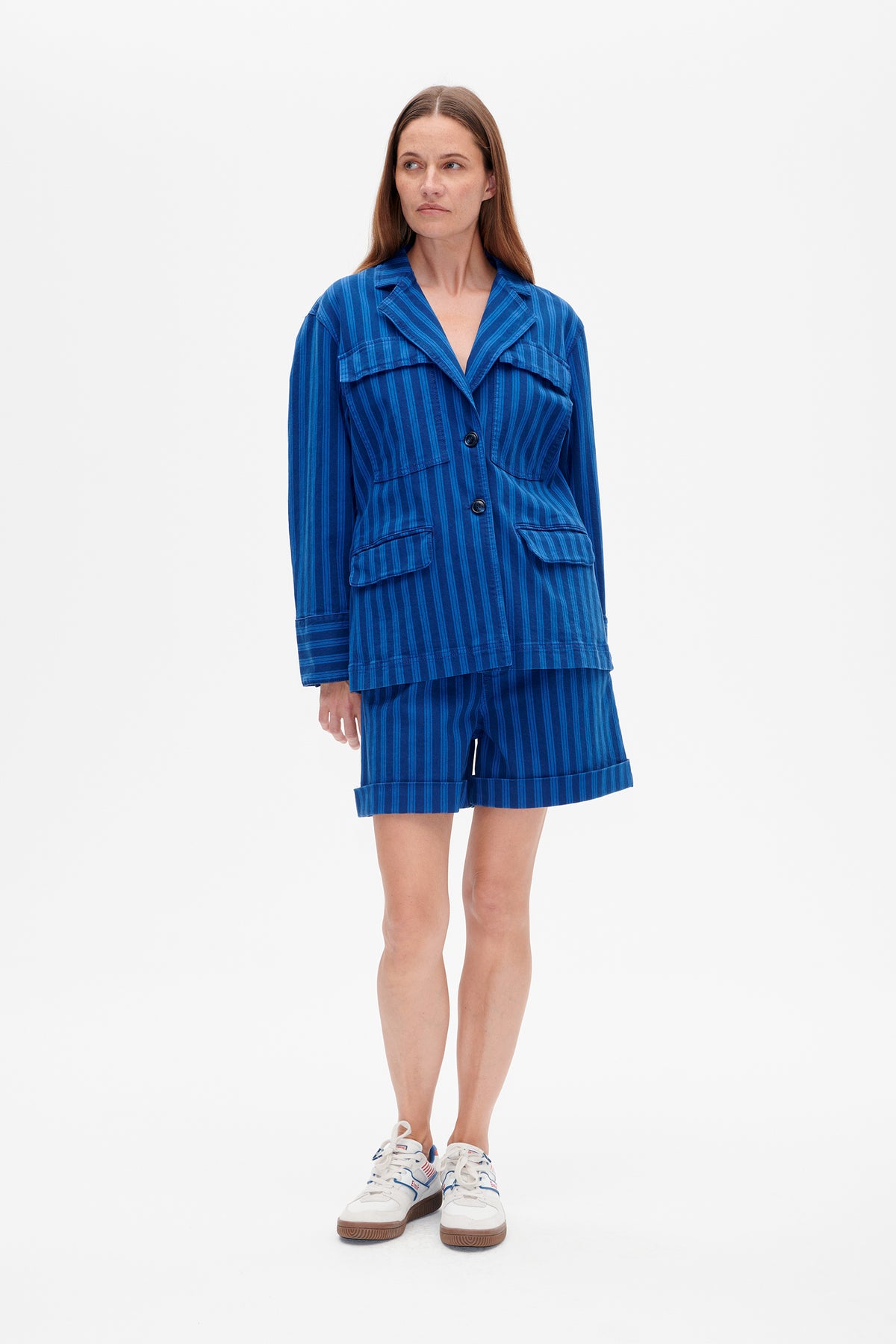 Model wearing a blue vertically striped button-front jacket with flap pockets and matching cuffed shorts, shown from the front.