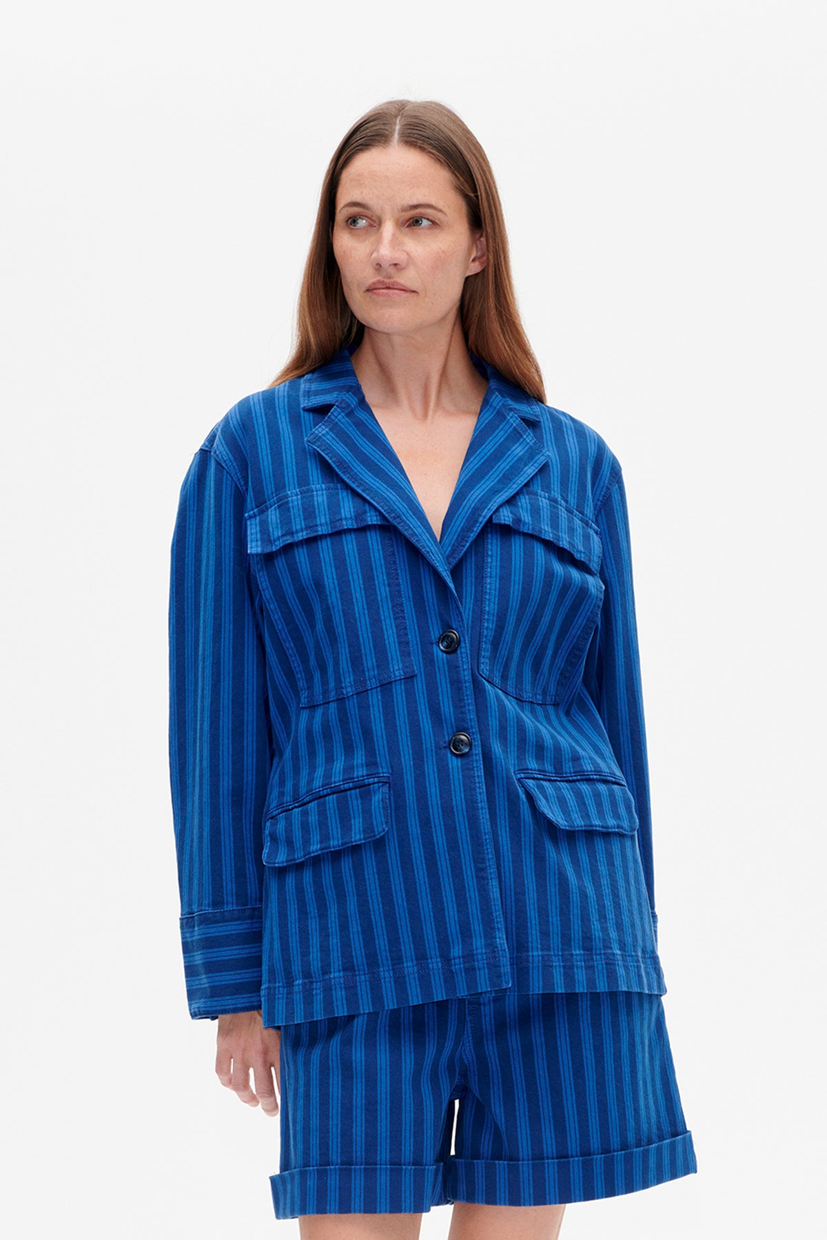 Front view of a model wearing a blue striped button-front jacket with a wide collar and flap pockets, paired with matching shorts.