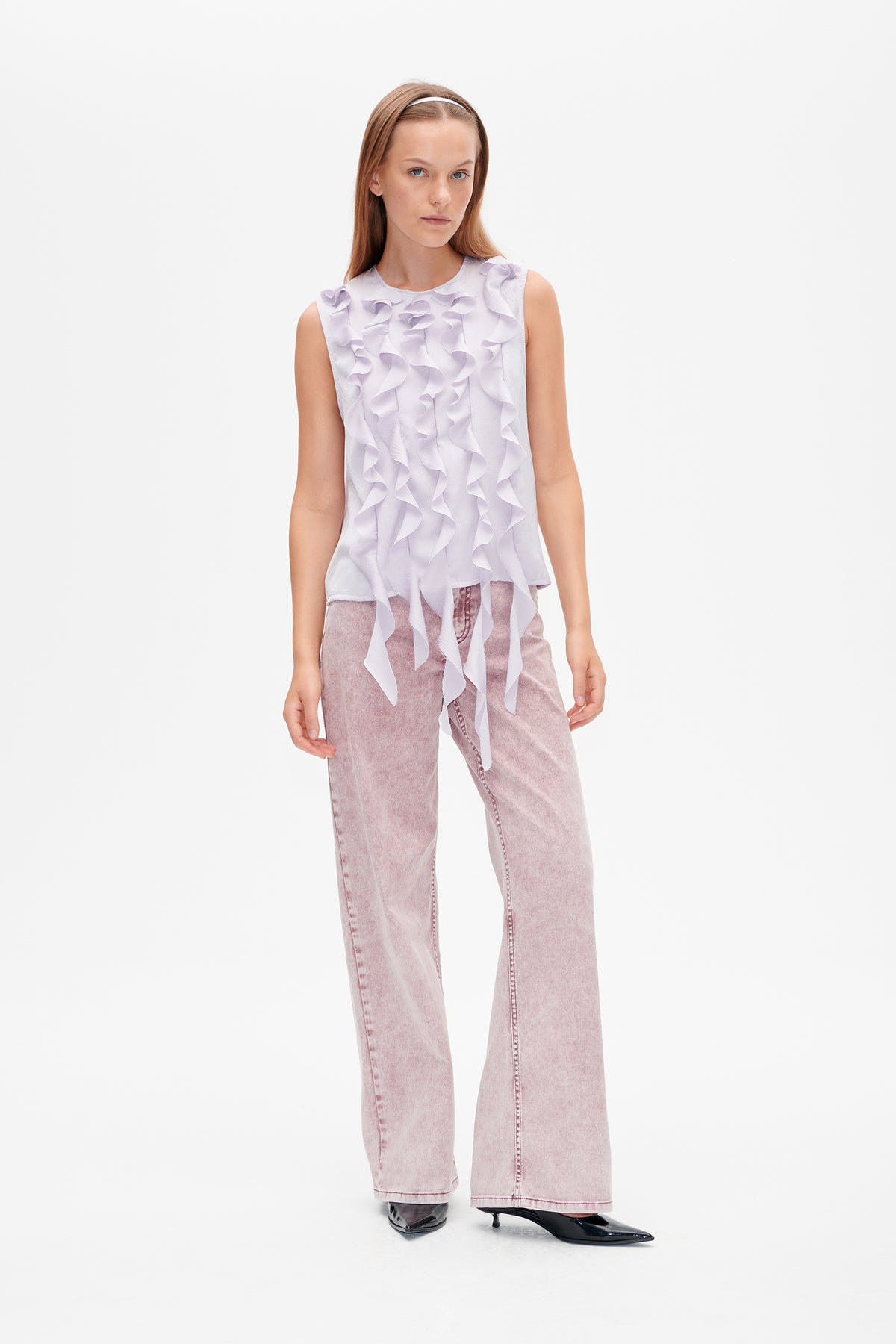 Model wearing a pale lilac sleeveless top with cascading ruffles and pink acid-wash wide-leg jeans, front view.