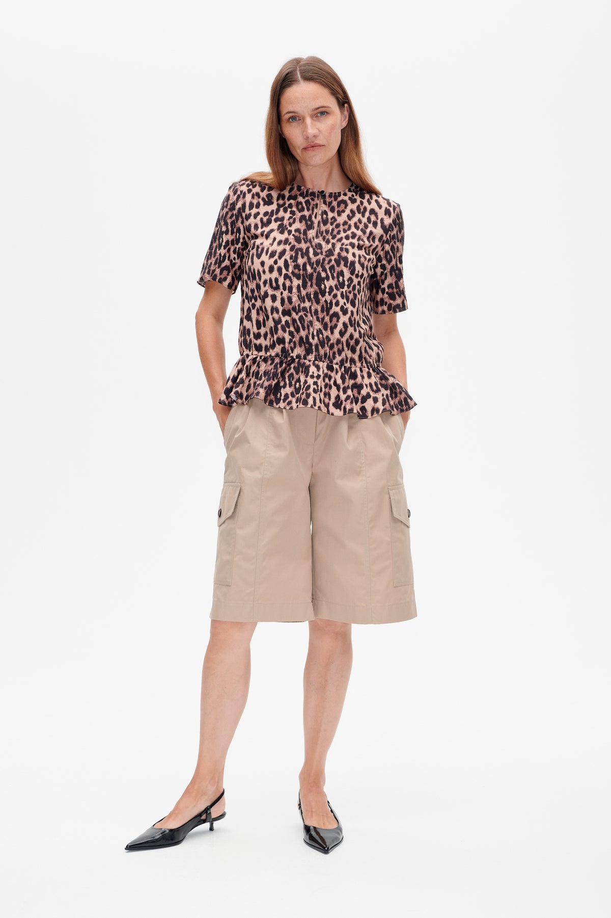 Front view of a model wearing a short-sleeved pink and brown leopard-print top with a flared peplum hem.