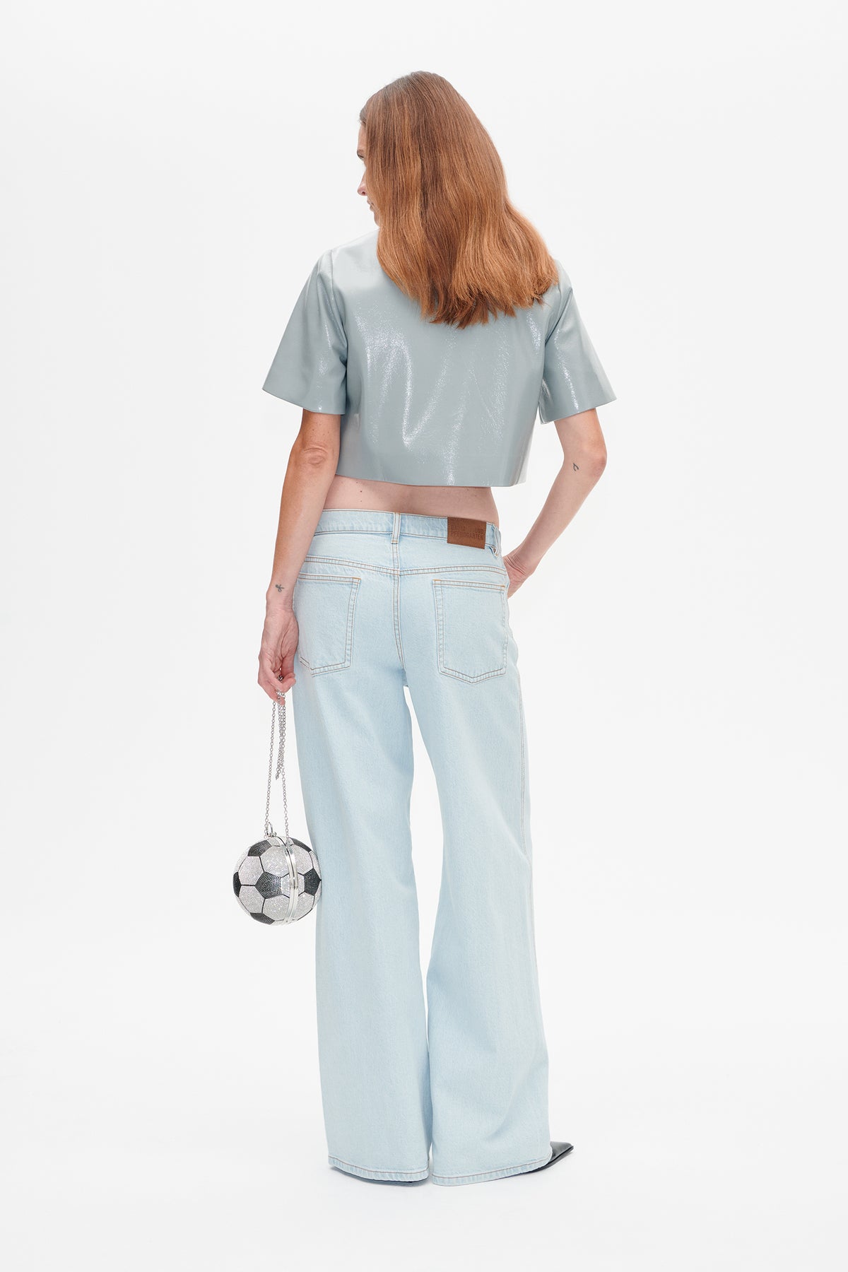 Back view of a glossy pale blue cropped short-sleeve top with light-wash wide-leg jeans.
