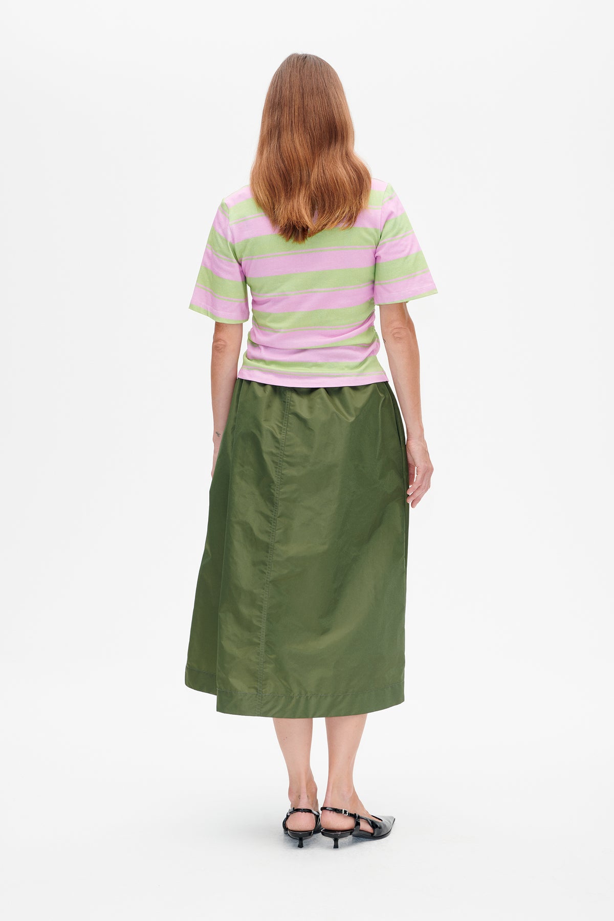 Rückenansicht eines Models in einem pink- und hellgrün gestreiften T‑Shirt mit kurzen Ärmeln und einem dunkelolivgrünen Midi‑Rock.