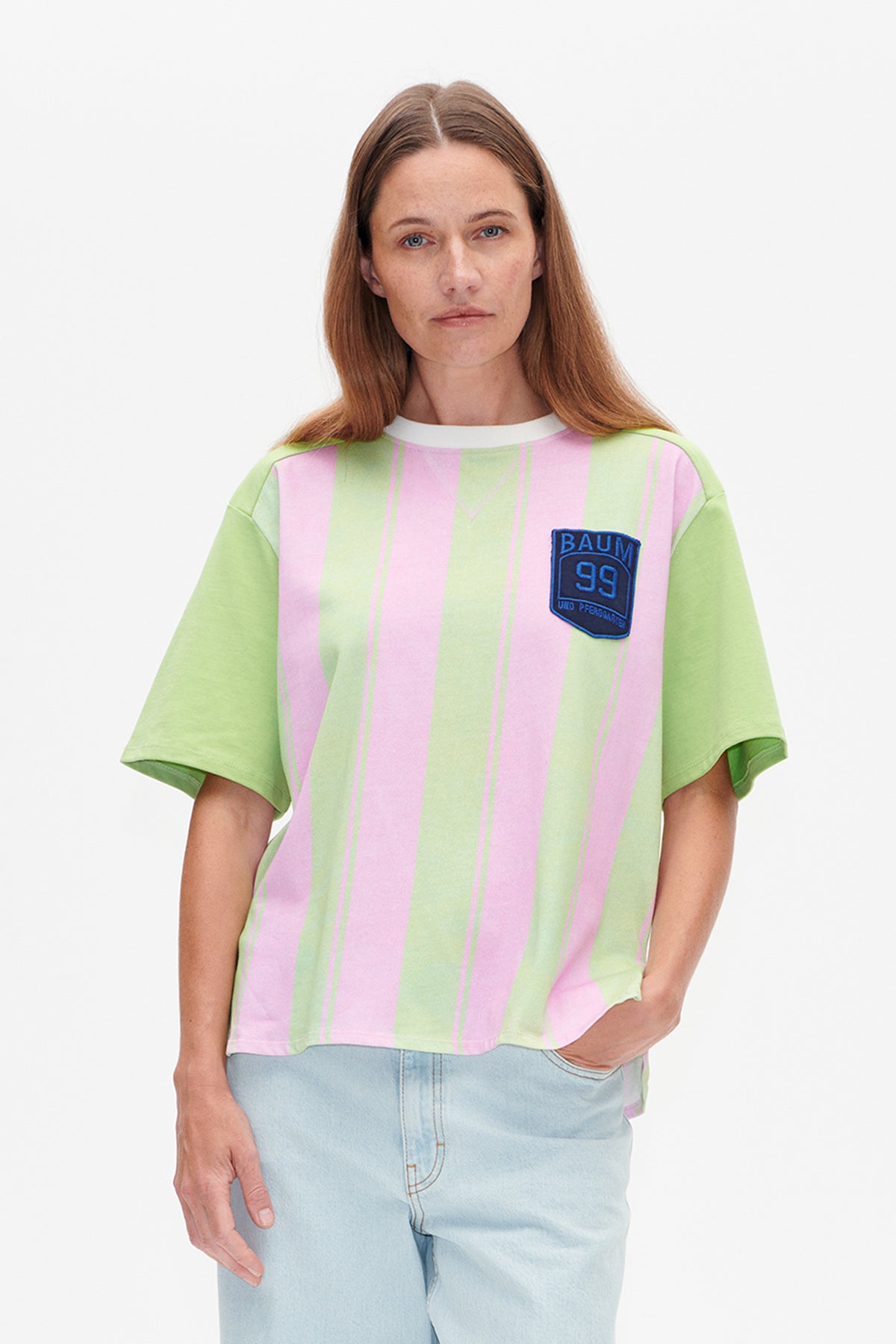 Vue de face d'un t-shirt à manches courtes et col rond, à rayures verticales rose et vert pâle, avec un écusson bleu sur la poitrine.