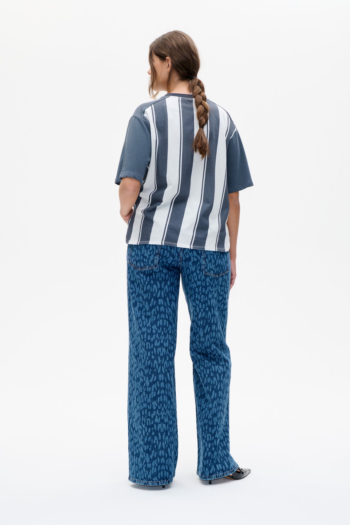 Back view of a model wearing a blue and white vertically striped short-sleeve T-shirt with patterned blue wide-leg jeans.