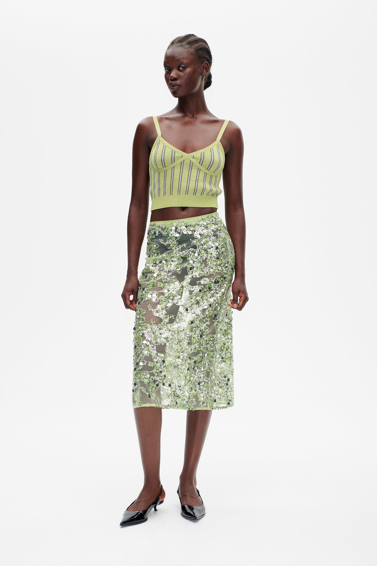 Vorderansicht einer limonengrünen, gestreiften Strick-Camisole, kombiniert mit einem transparenten Midirock, der mit grünen und silbernen Pailletten bedeckt ist.